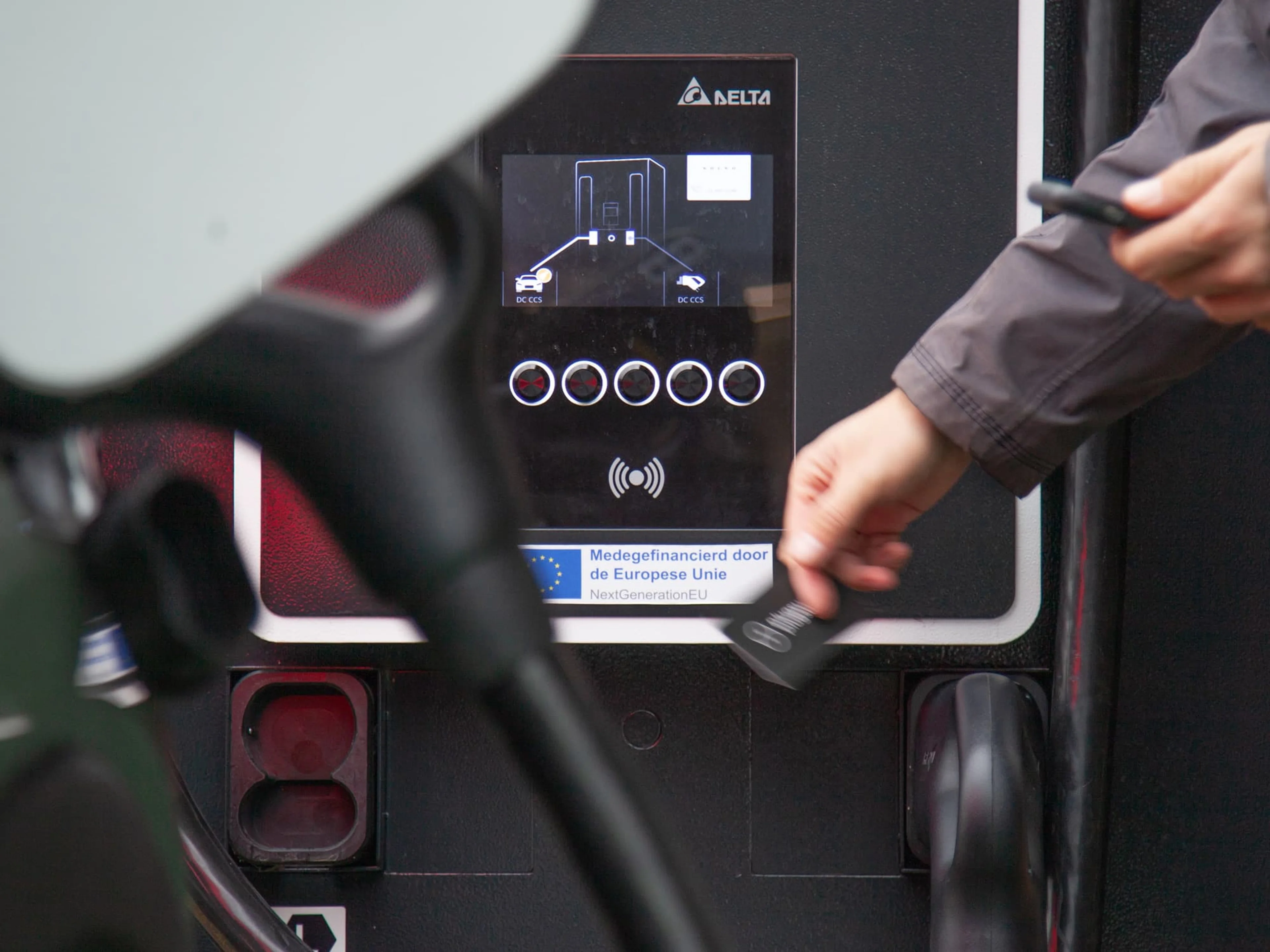 Une personne présente une carte Plugsurfing devant le terminal de paiement d'une borne de recharge.