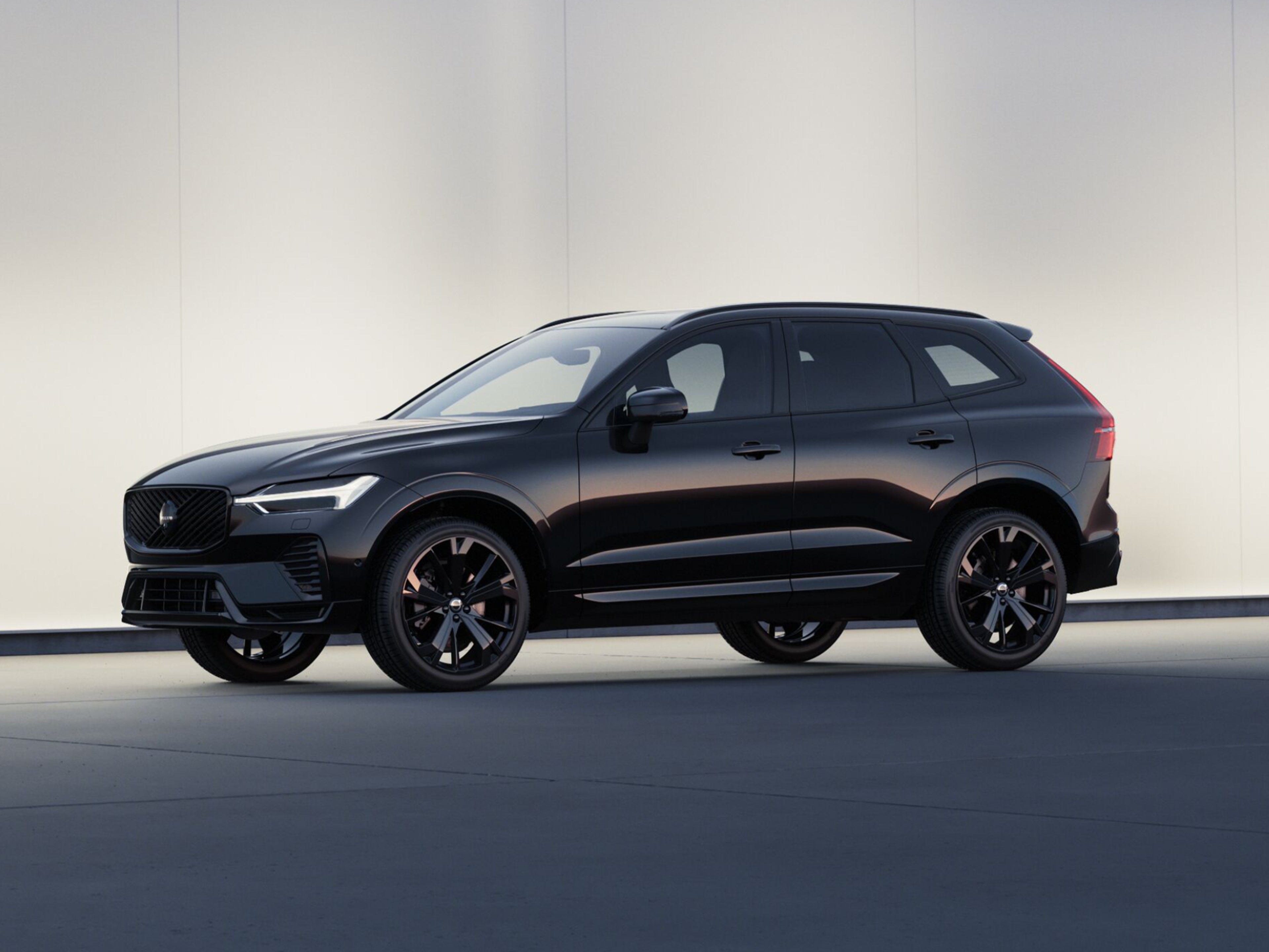 Seitenansicht eines tiefschwarzen Volvo XC60 SUV vor einer hellen Steinwand.