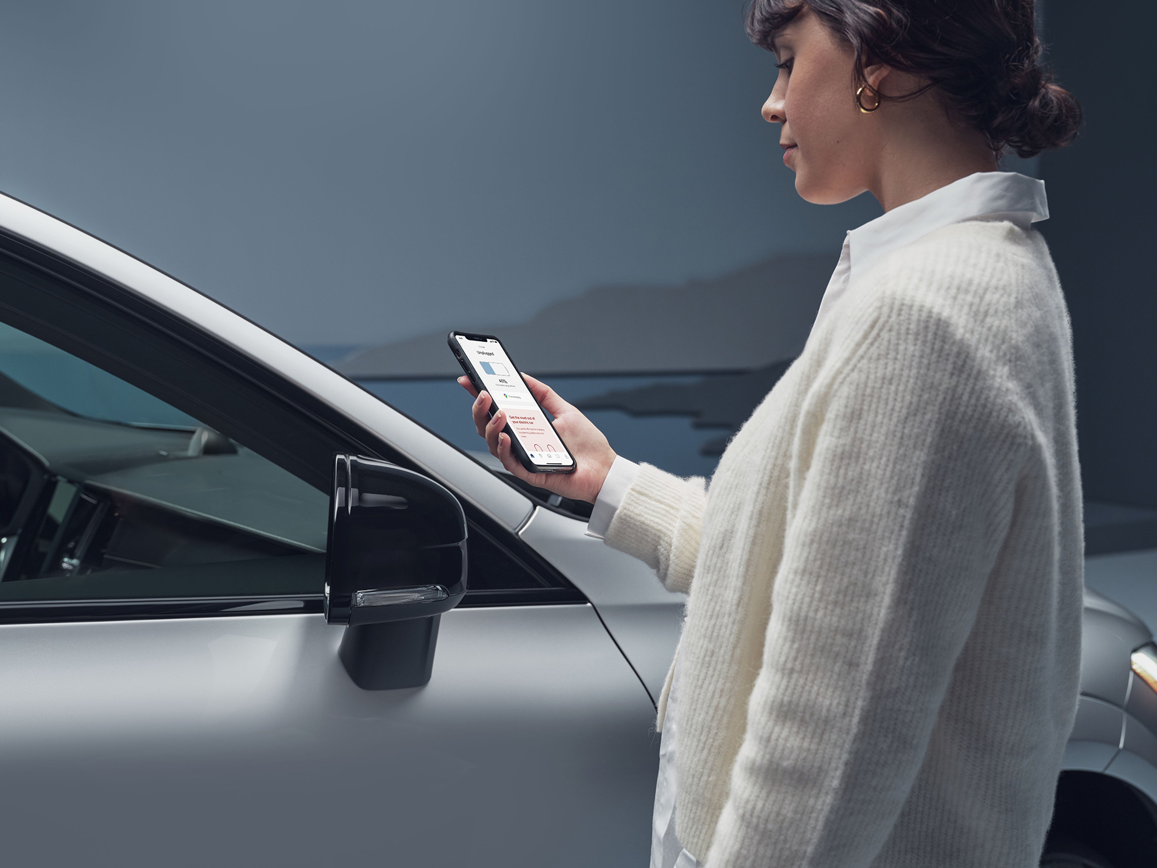 Une femme demande une assistance routière au moyen de son téléphone portable à partir de l’application Volvo Cars