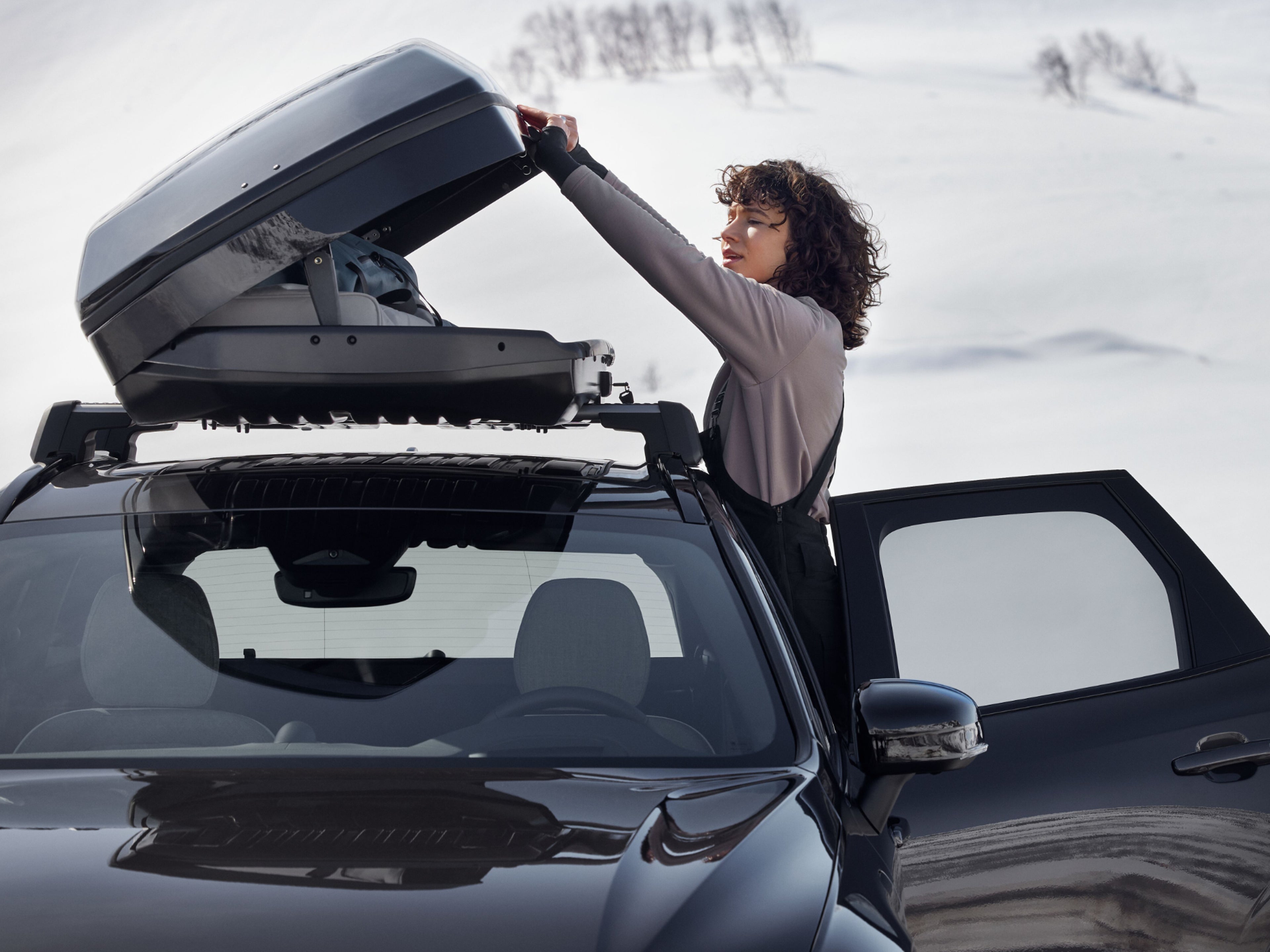 Eine Frau öffnet eine Dachbox, welche auf einem Fahrzeug befestigt ist.