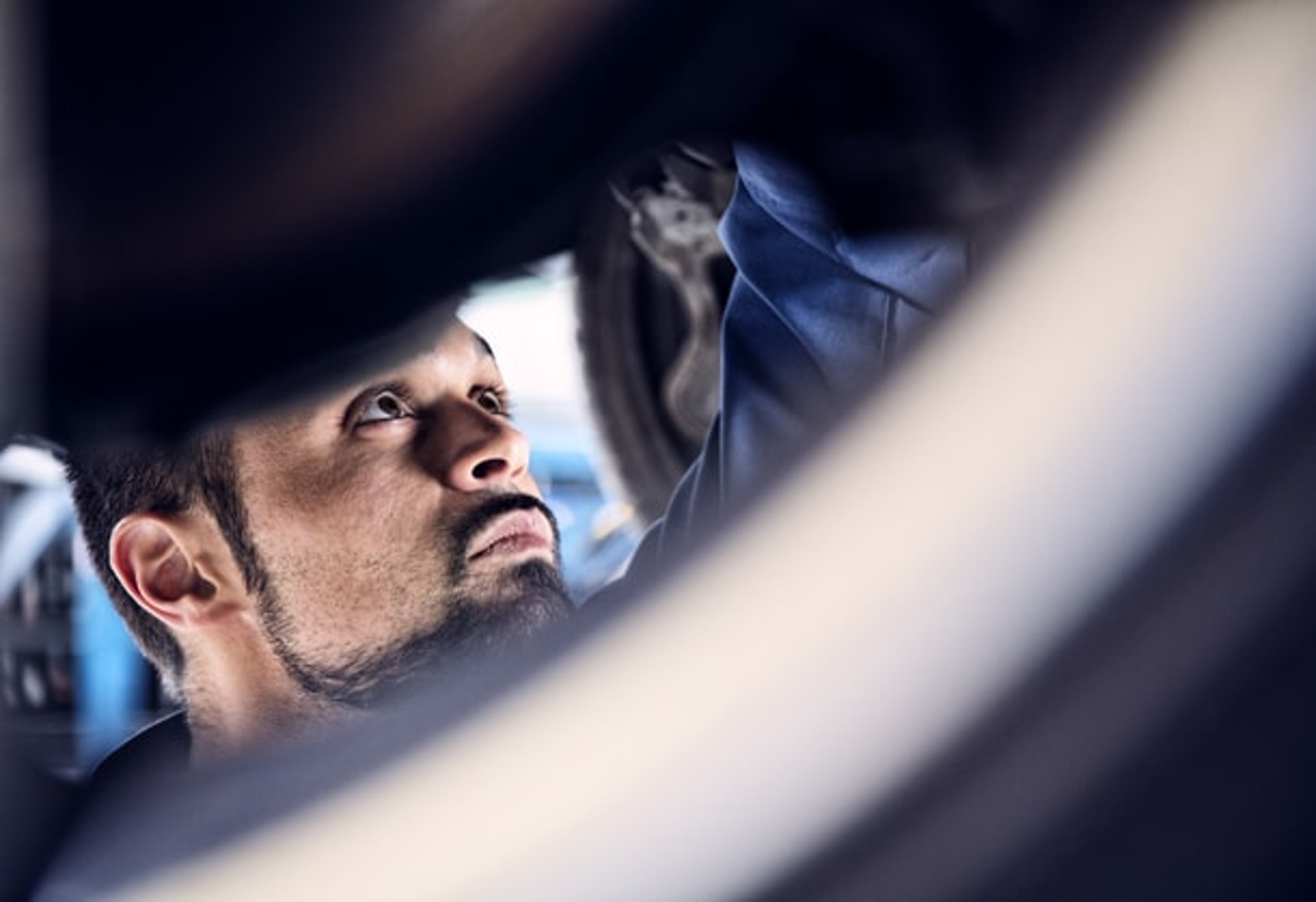 En fokuseret Volvo mekaniker inspicerer bilens undervogn, synlig gennem en hjulfælgsåbning. Lyset er blødt og fremhæver hans koncentration og ekspertise.