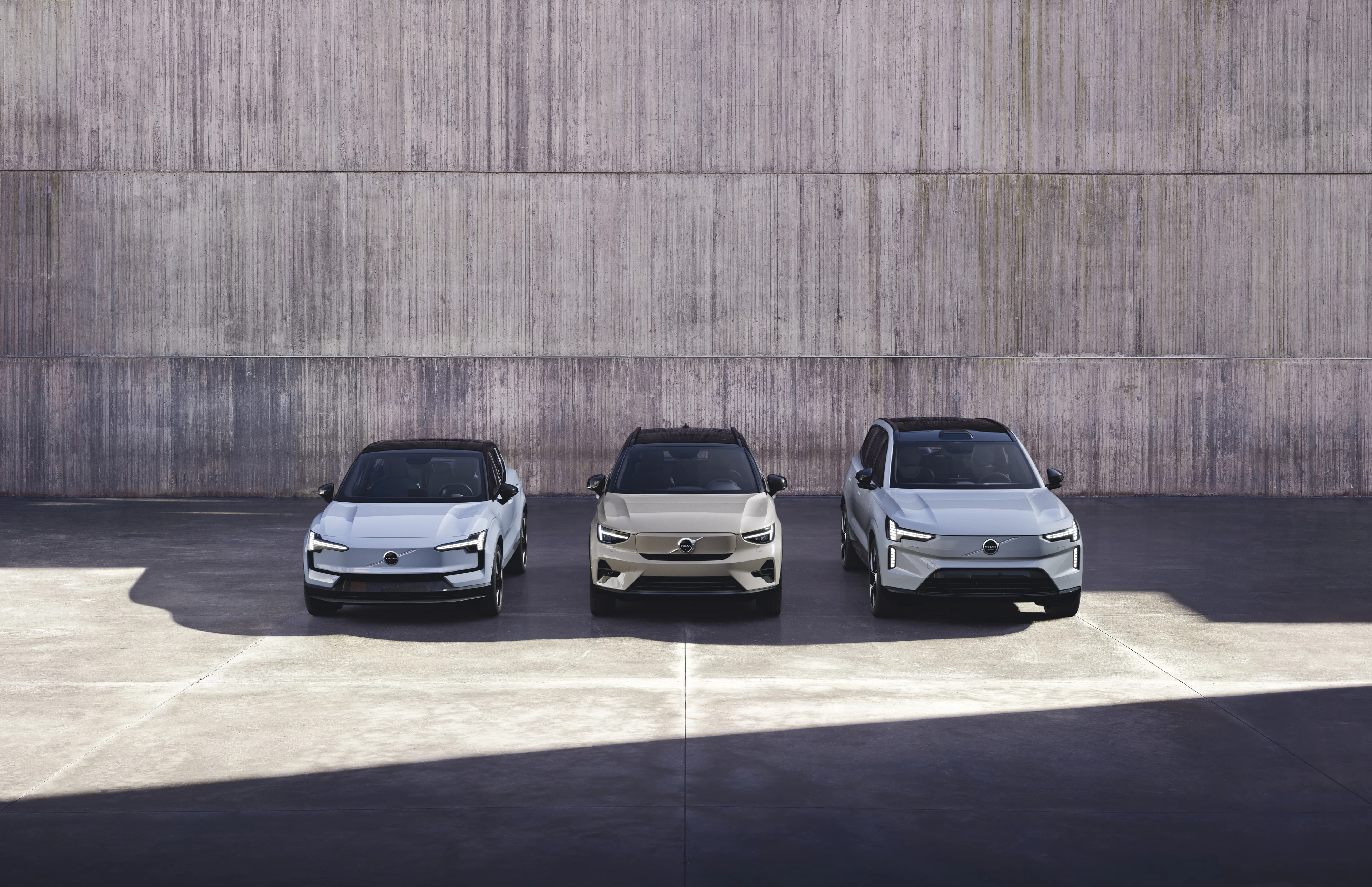 Three Volvo cars in a row against a grey block wall.