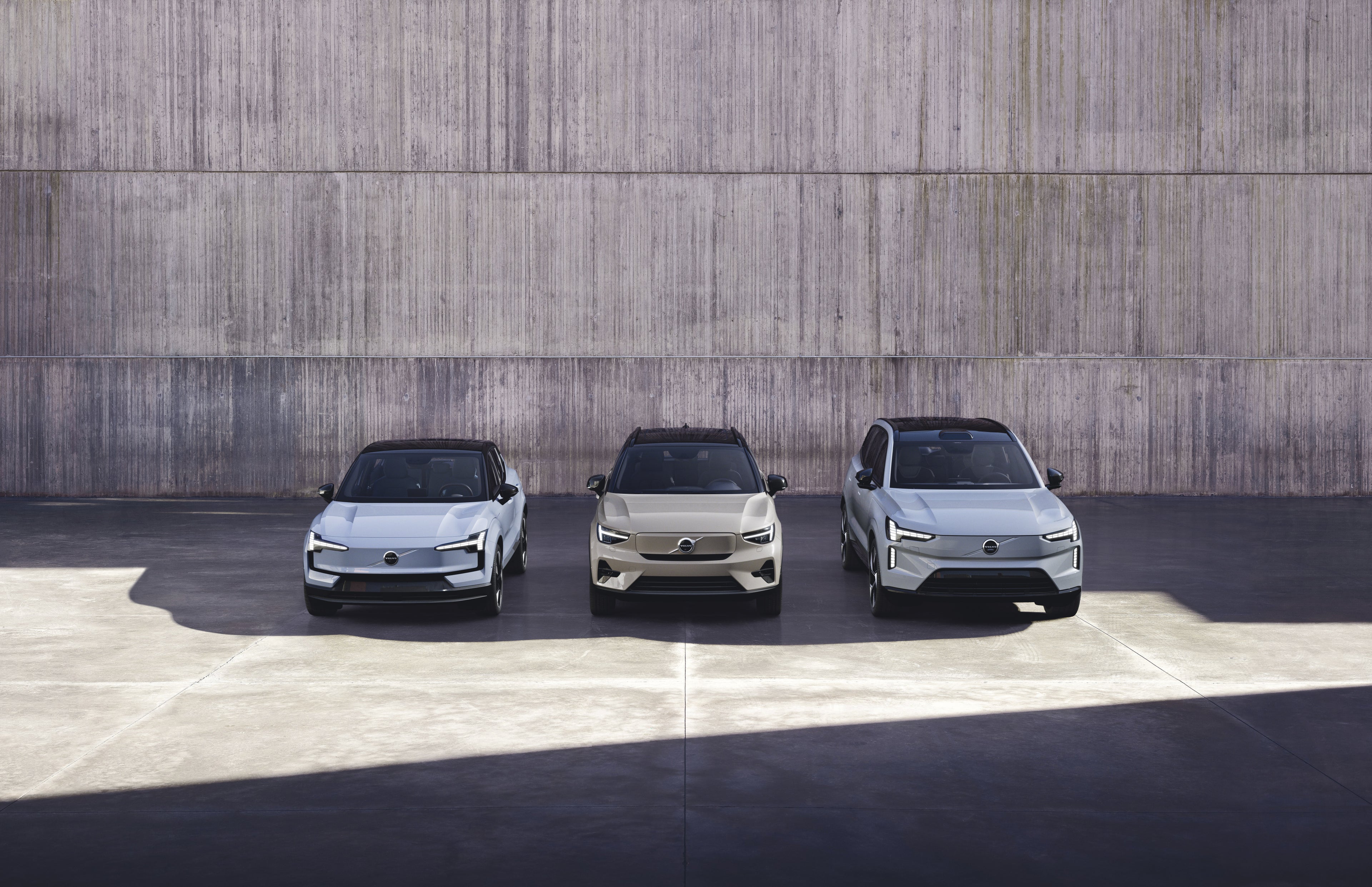 Three Volvo cars in a row against a grey block wall.