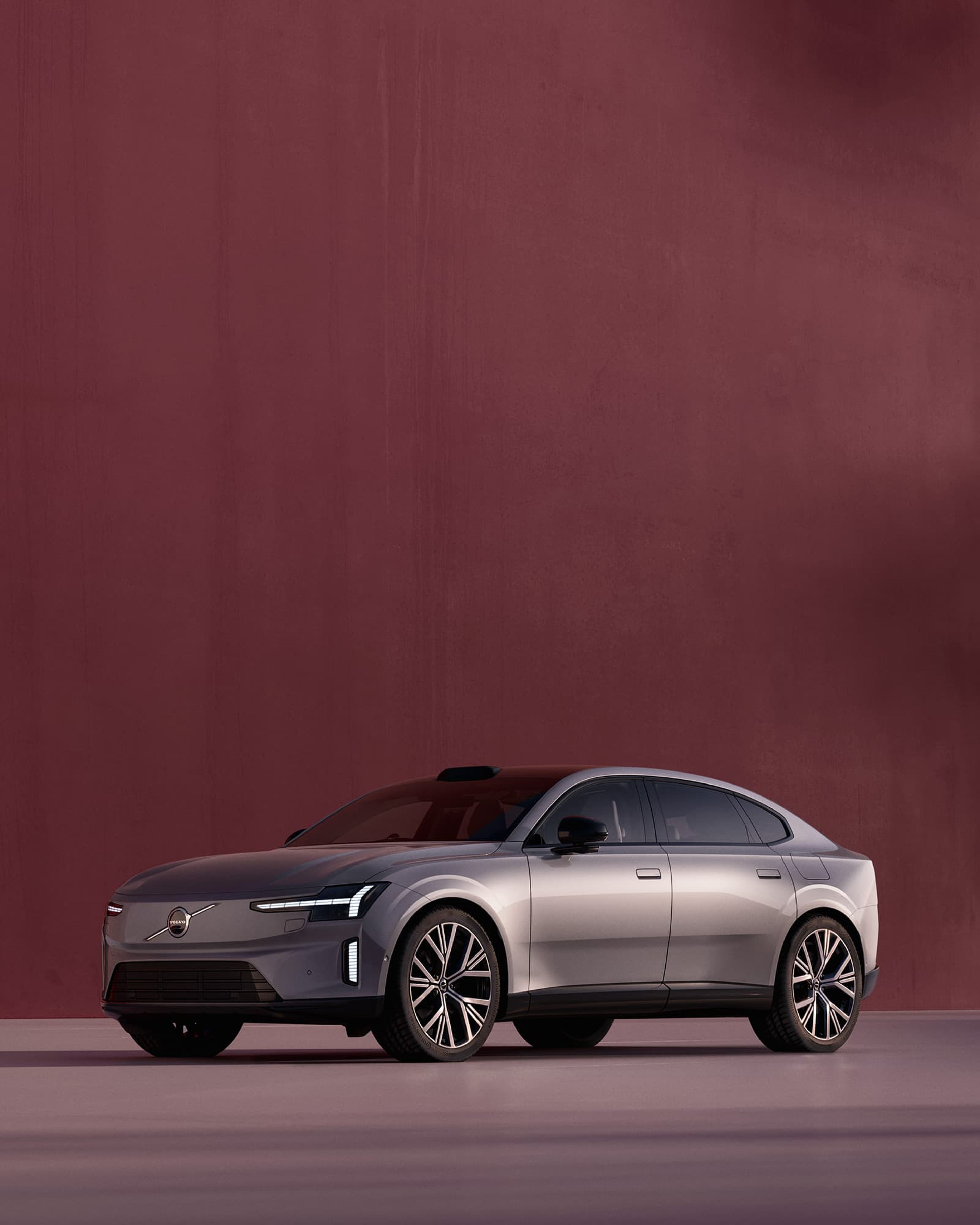 Zijaanzicht van een grijze Volvo ES90 op een bordeaux achtergrond.