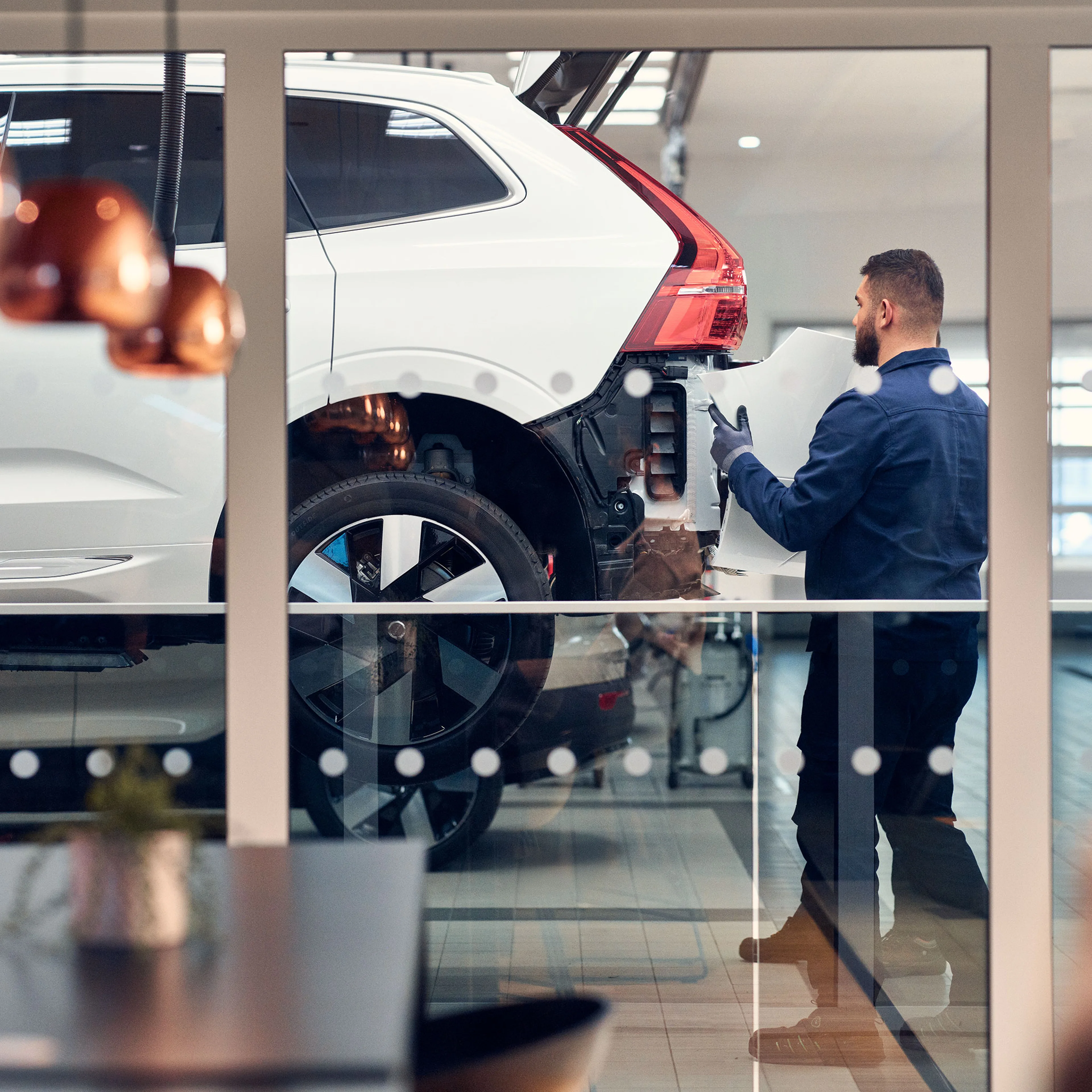 Volvo Personal Service huollon odotustilan lasin läpi näkyvä Volvo Omamekaanikko työstää huollettavan Volvon takapuskuria.
