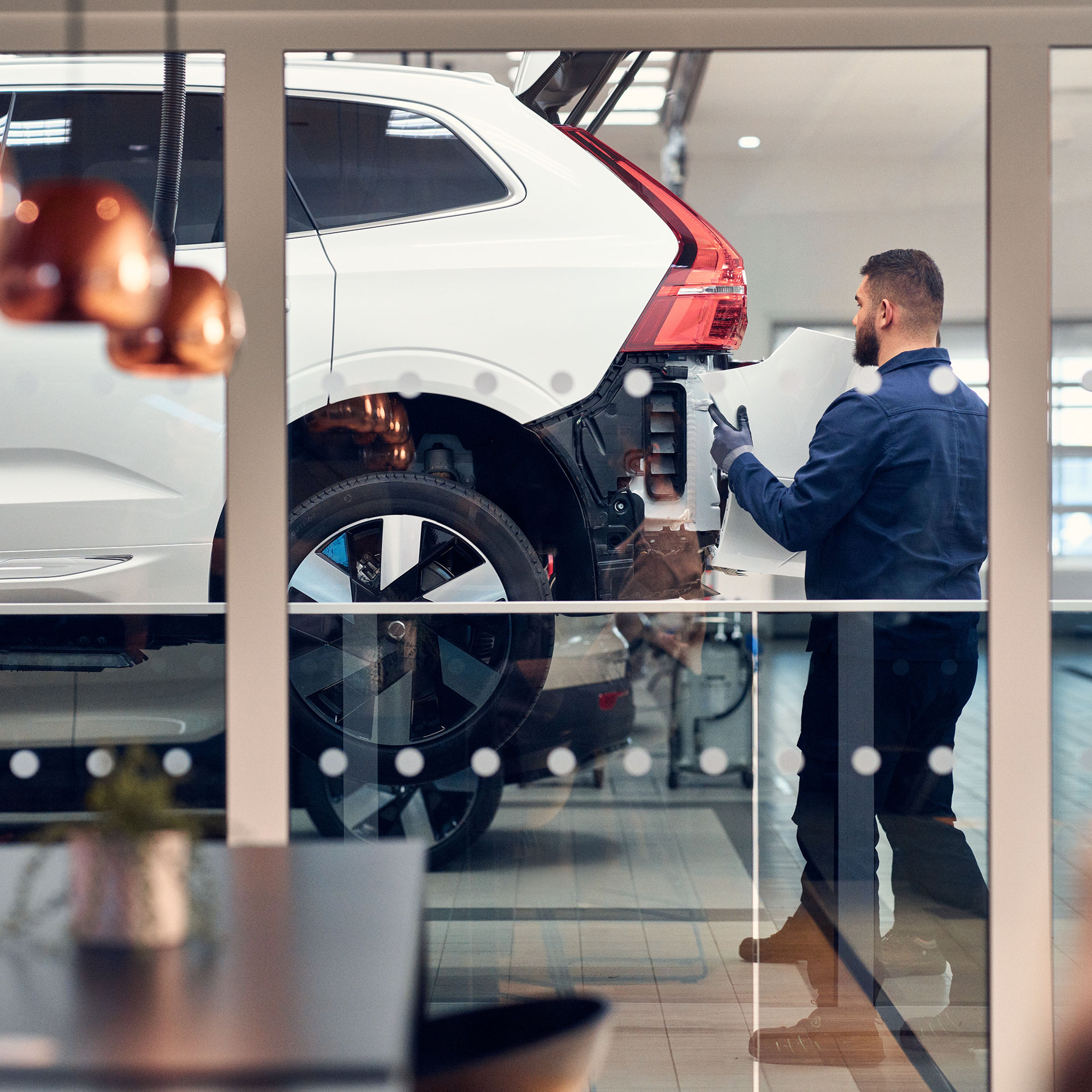 Volvo Personal Service huollon odotustilan lasin läpi näkyvä Volvo Omamekaanikko työstää huollettavan Volvon takapuskuria.