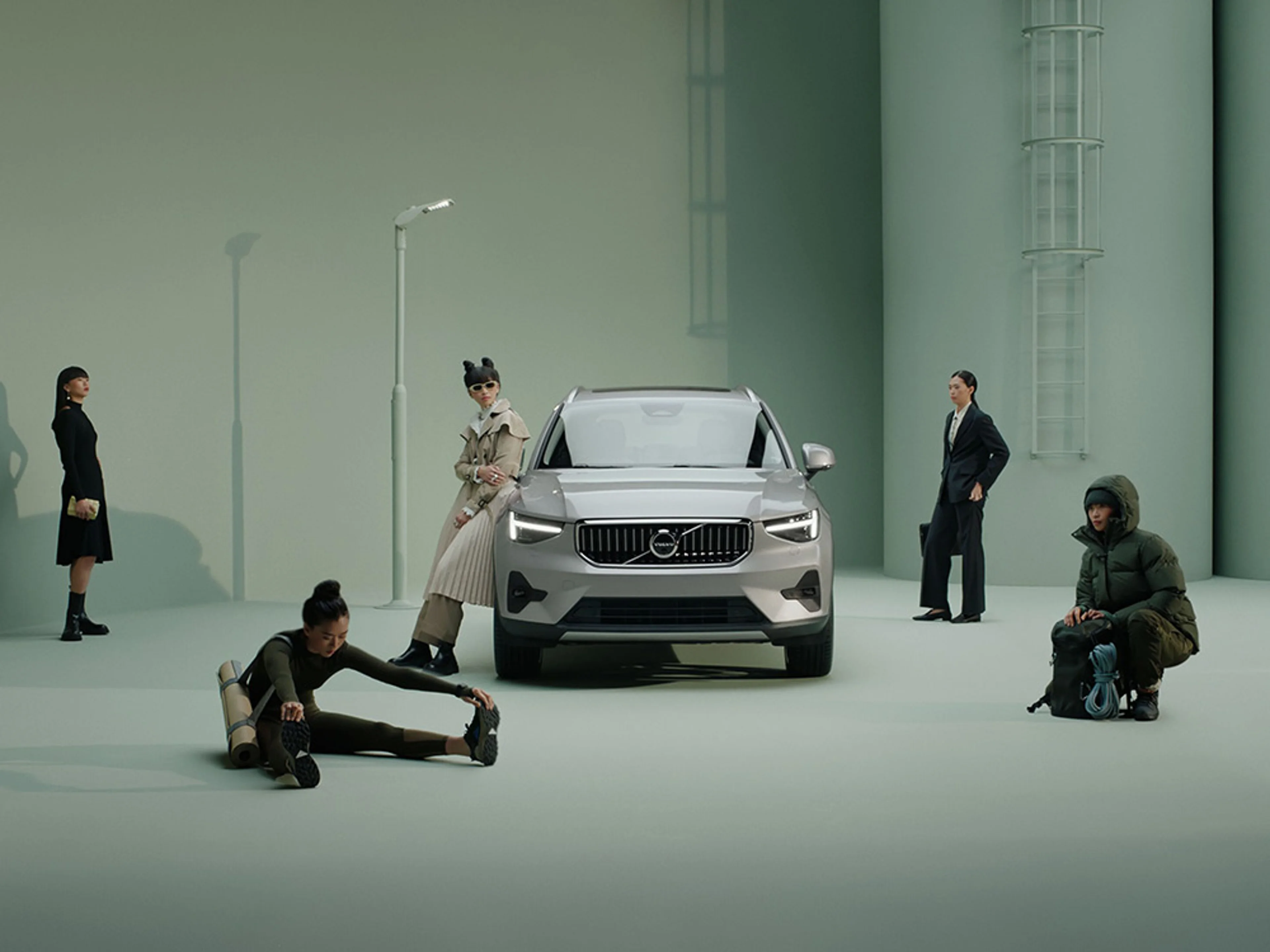 Plusieurs personnes portant des tenues différentes entourent une Volvo EX40 argentée sur un fond de studio vert.