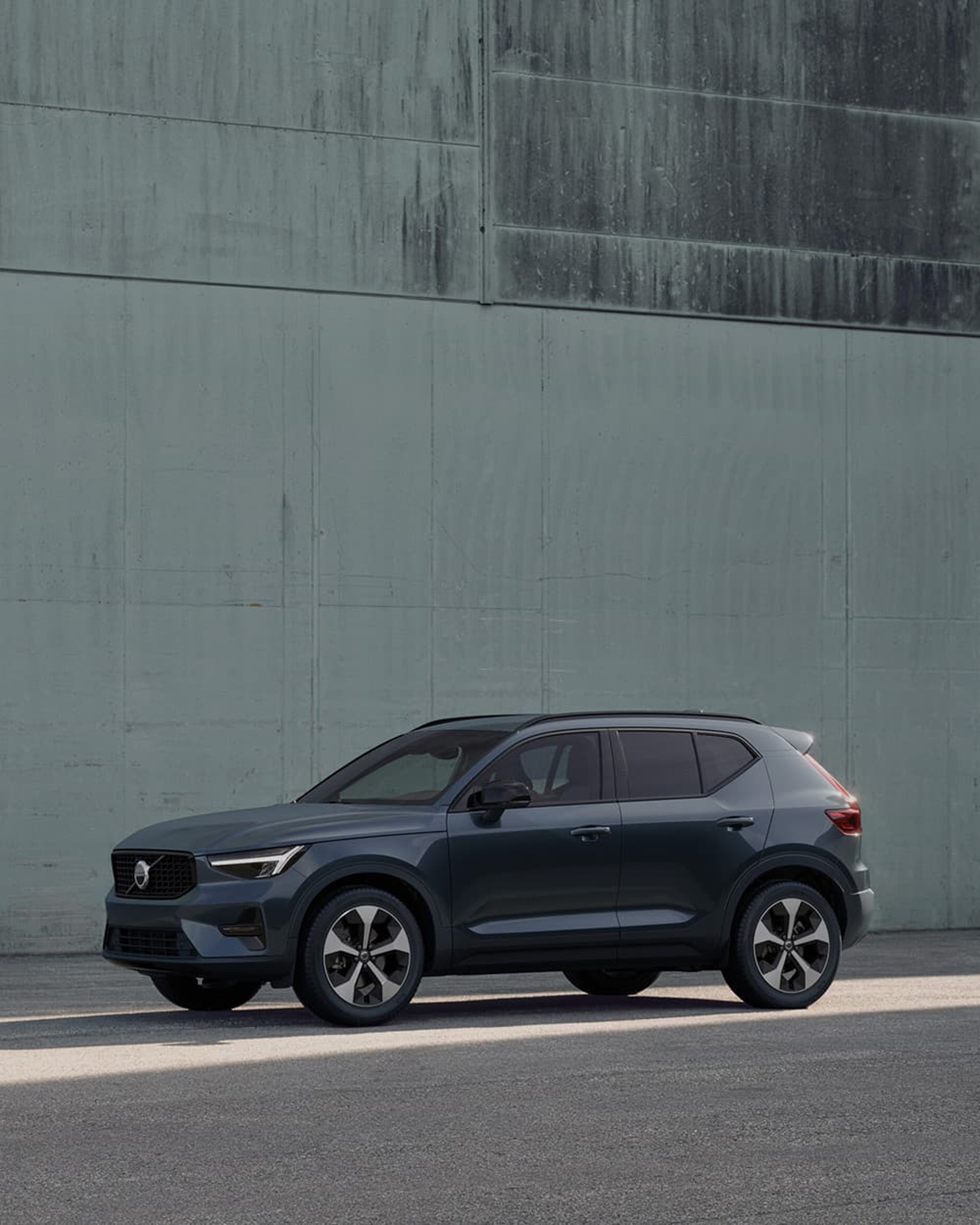 Une Volvo XC40 foncée garée contre un mur vert