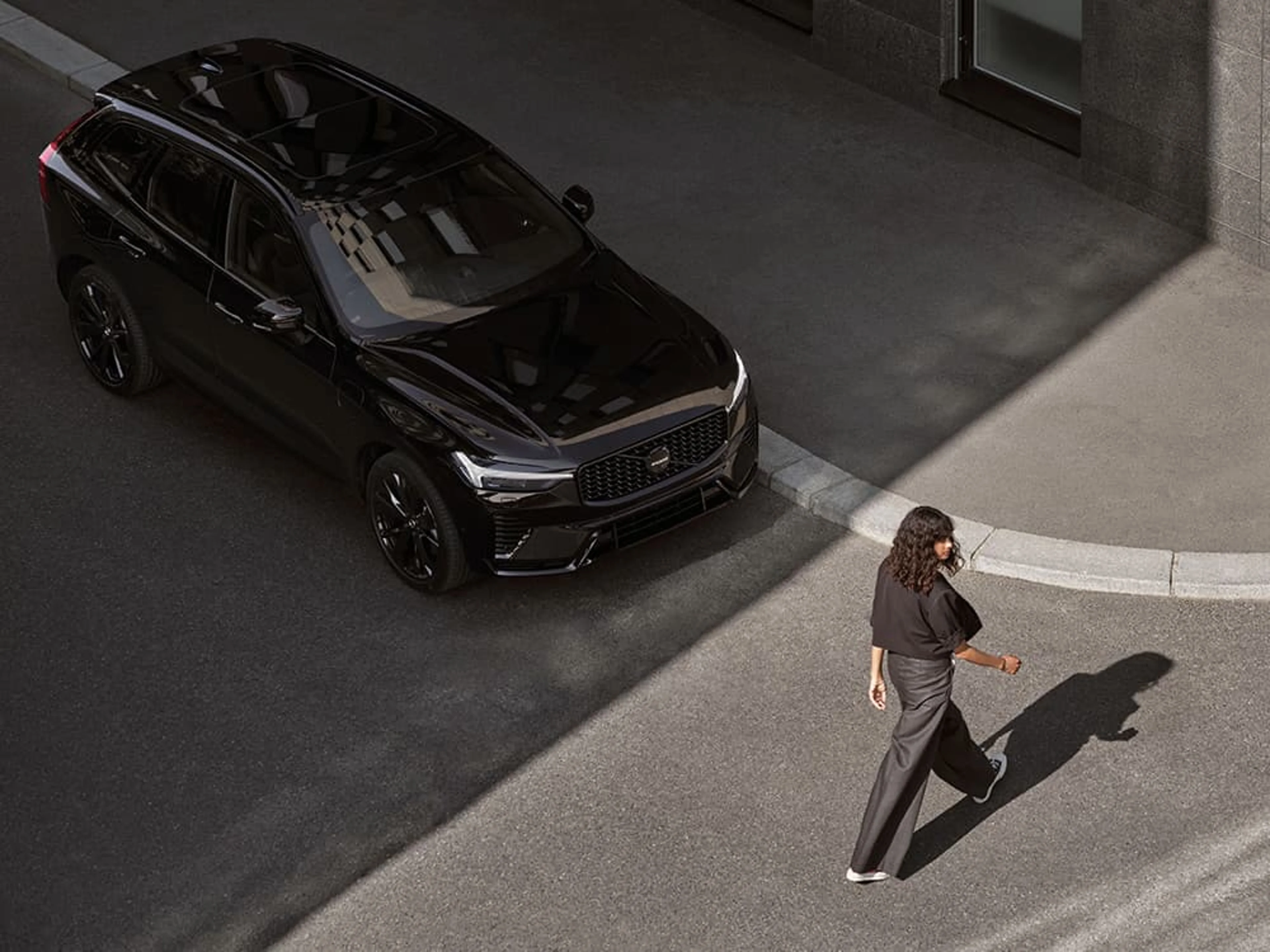Une femme traverse la rue alors qu'une Volvo XC90 noire l'attend.