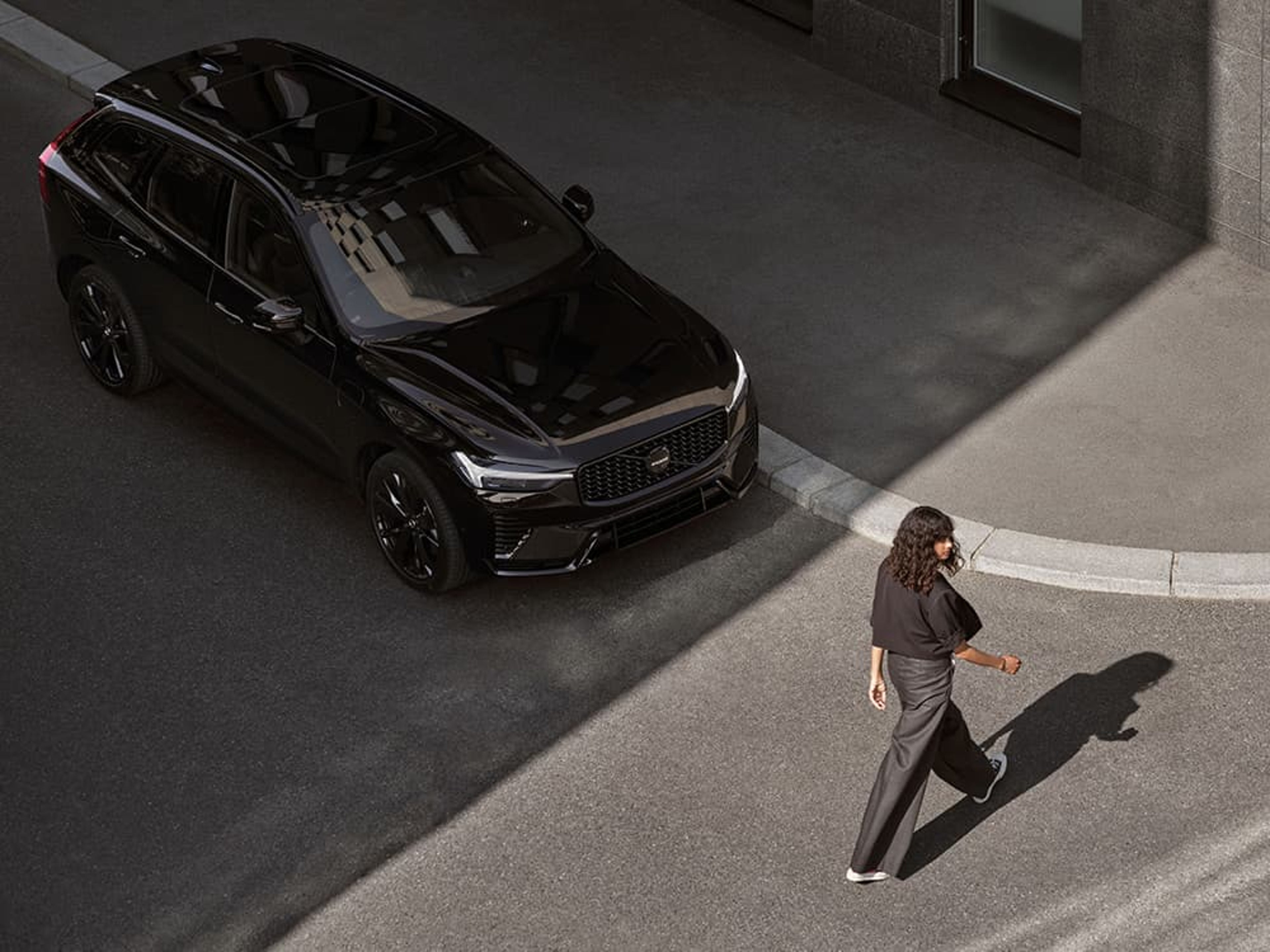 Une femme traverse la rue alors qu'une Volvo XC90 noire l'attend.