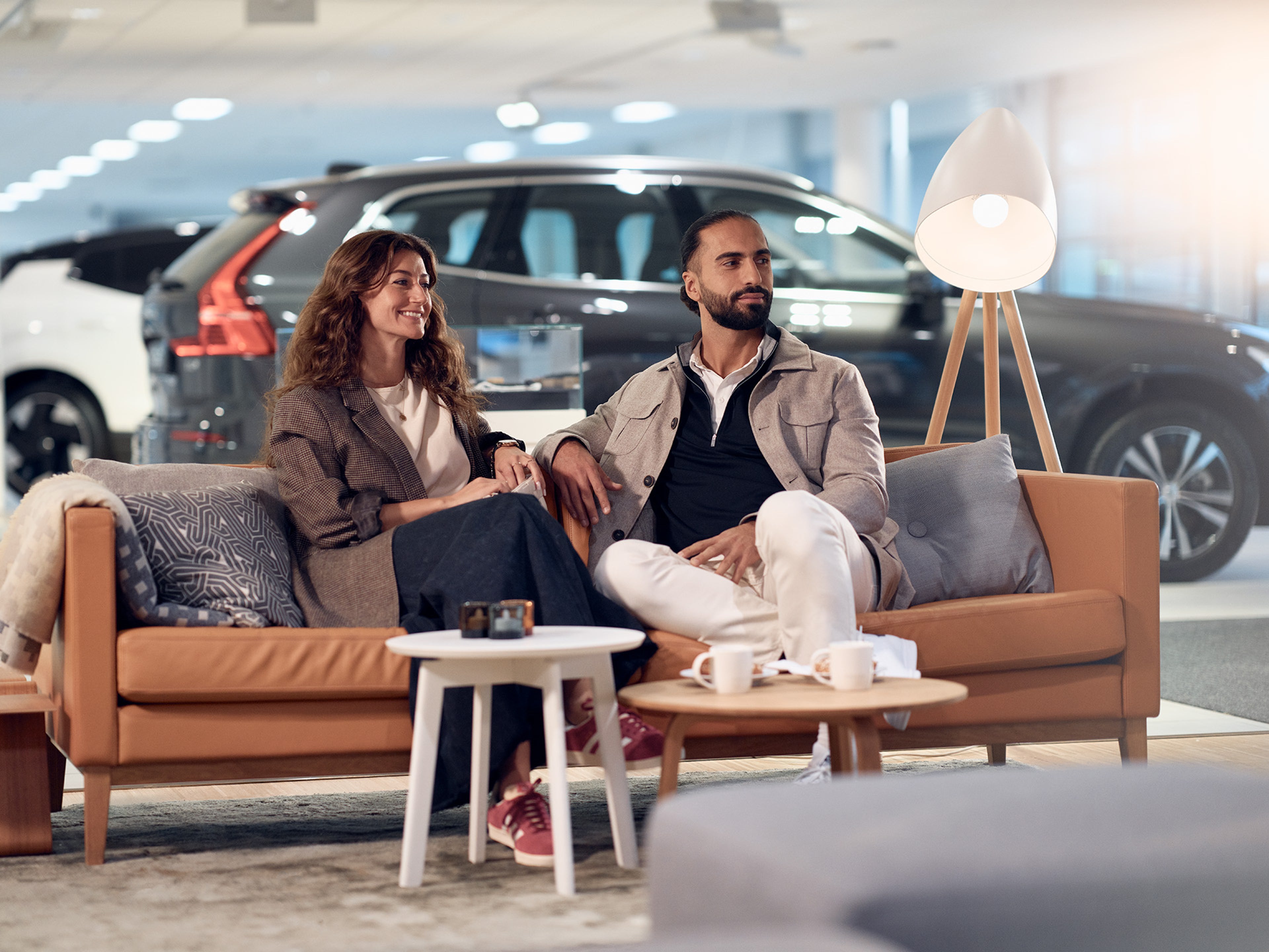 Casal sentado em sofá dentro de um concessionário, com Volvos ao fundo.