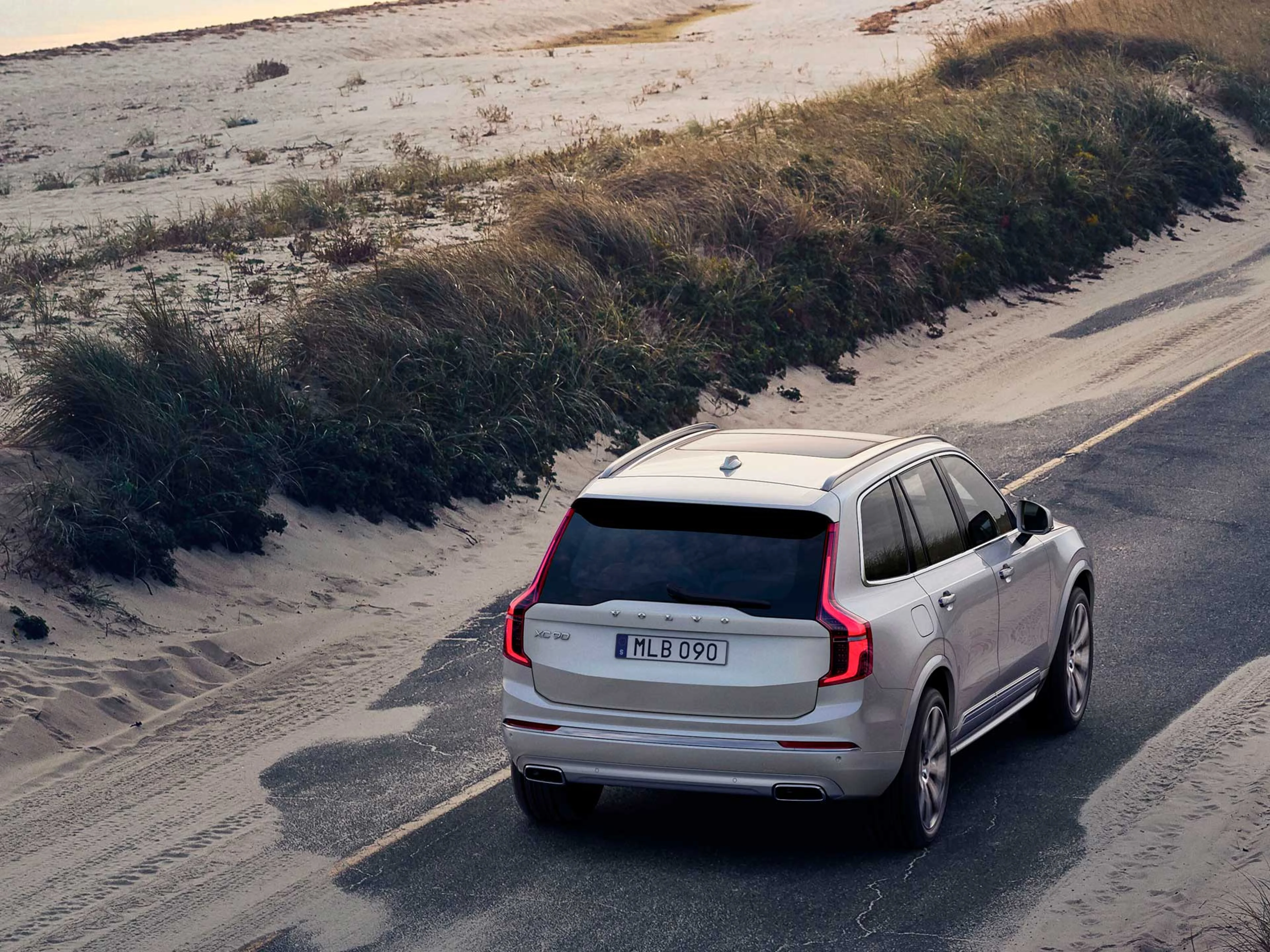 Un XC90 sobre un camino a la orilla de mar con arena.