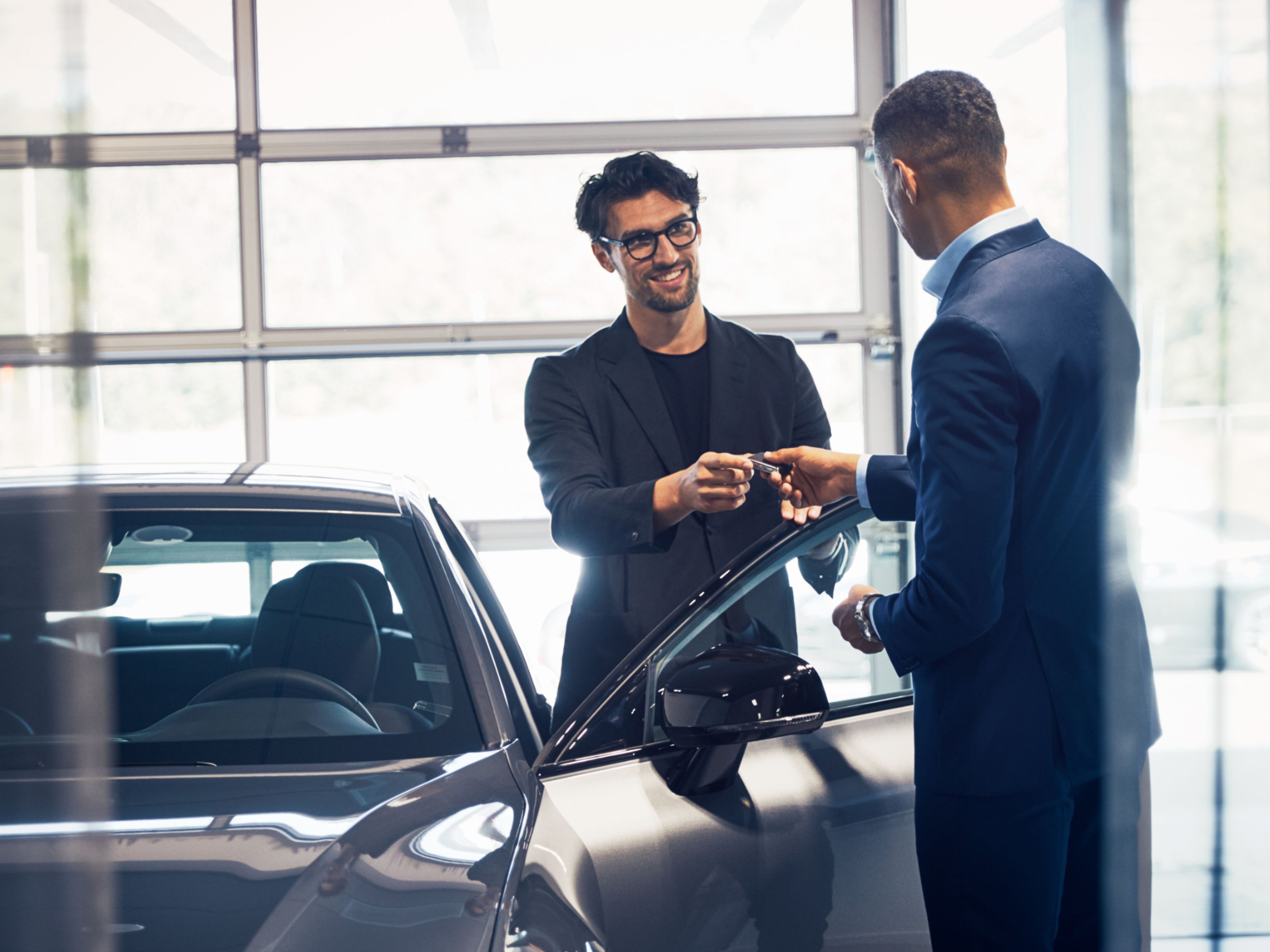 Ein männlicher Volvo Kundenberater übergibt einem männlichen Kunden den Schlüssel zu einem Volvo in einem Showroom.