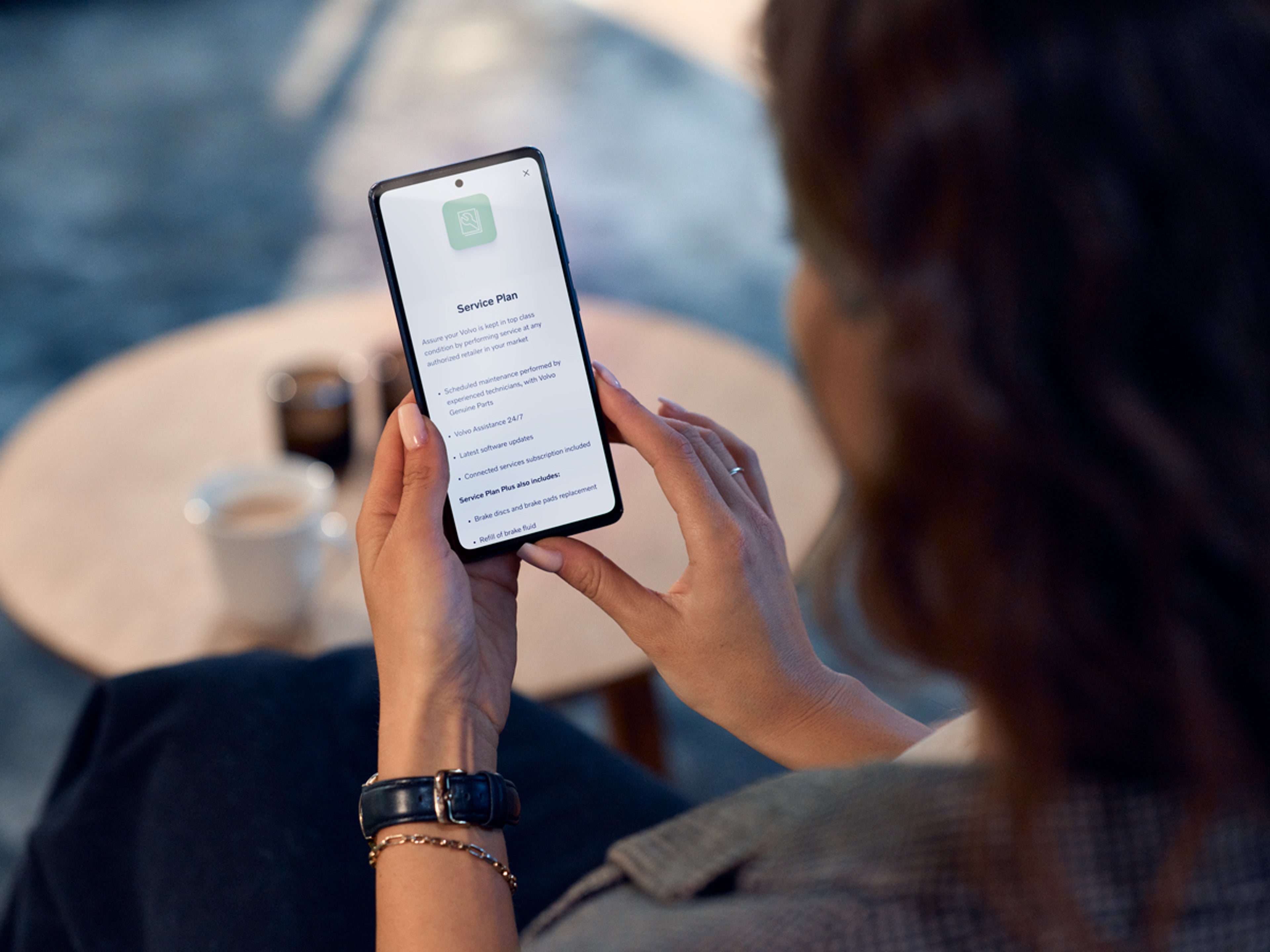 Kvinna håller en mobiltelefon som visar Serviceavtal i Volvo Cars appen