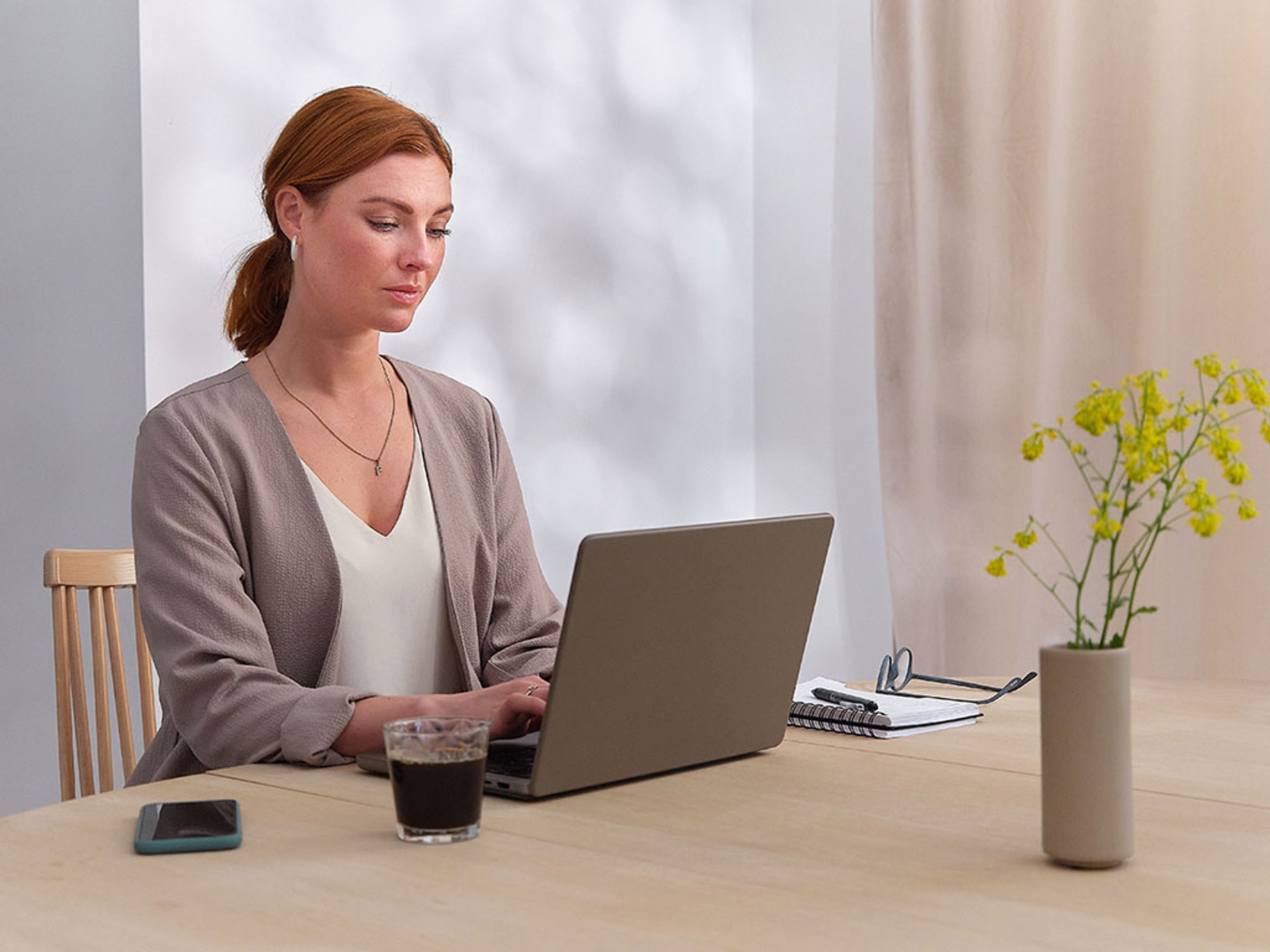 Femme travaillant sur un ordinateur portable à une table avec smartphone, carnet, stylo, verre et vase avec fleurs
