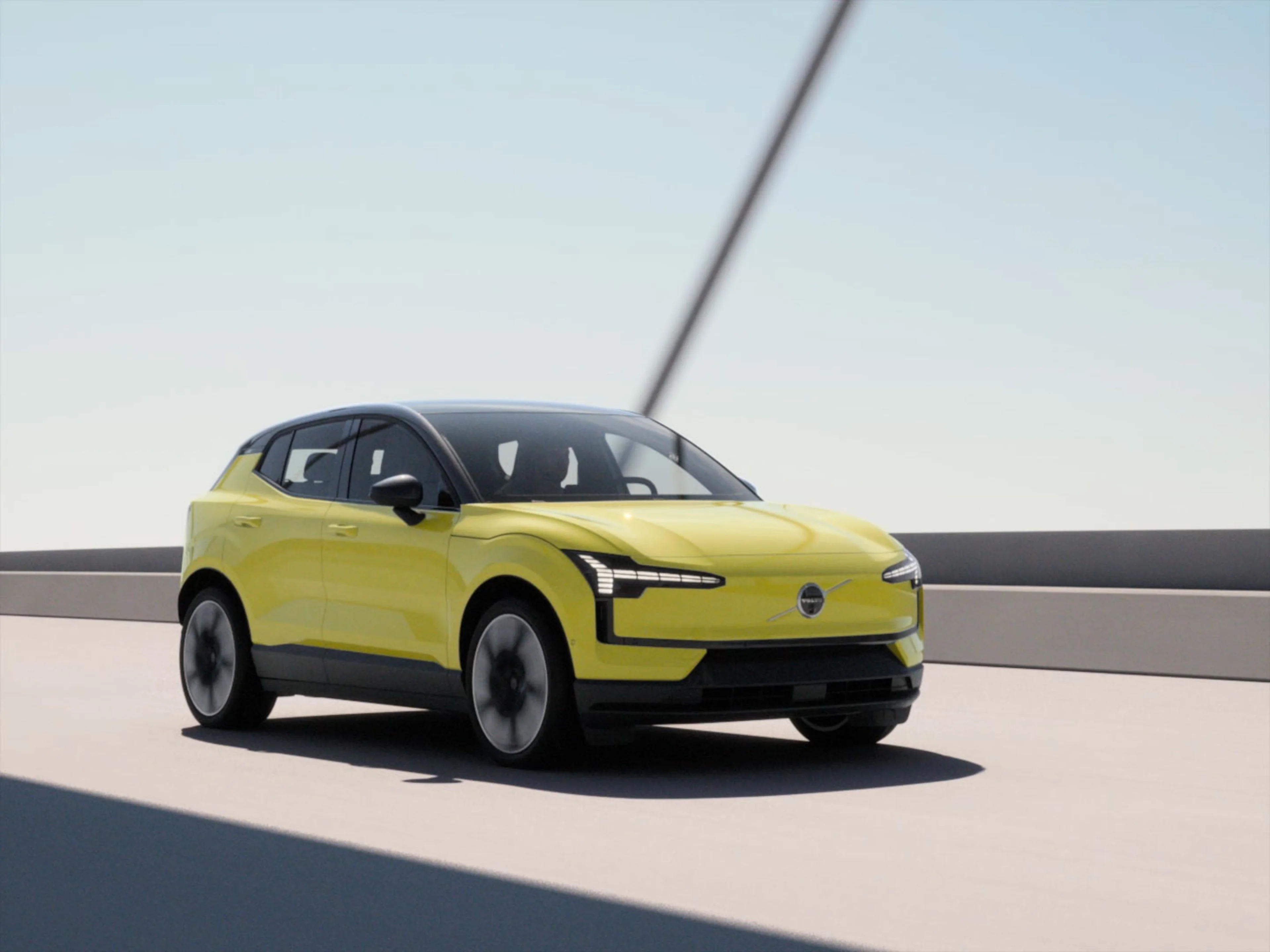 Voiture Volvo EX30 électrique jaune vif roulant sur une route ensoleillée sous un ciel bleu clair.