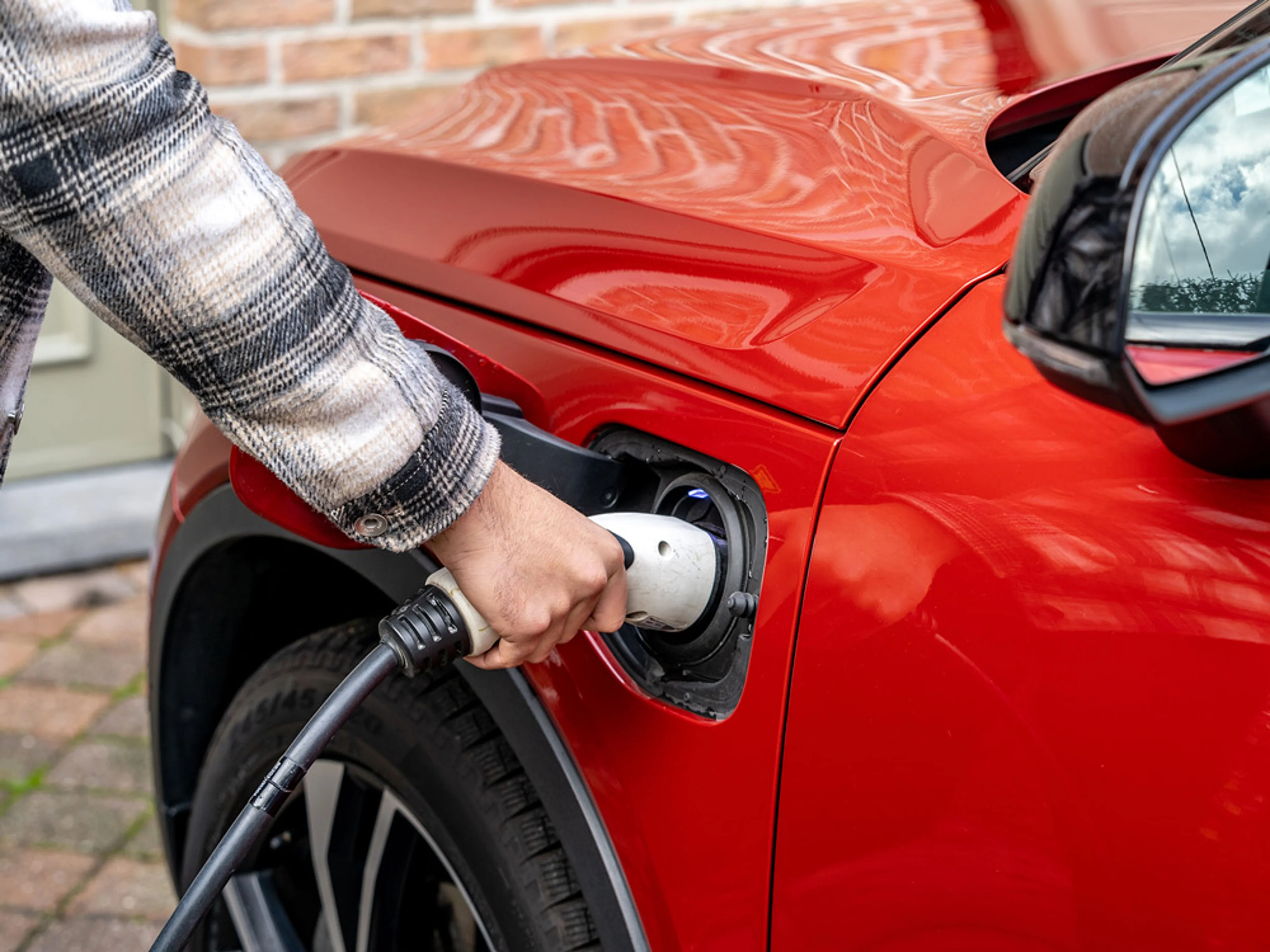 Une personne branche un câble de recharge dans une Volvo électrique rouge.
