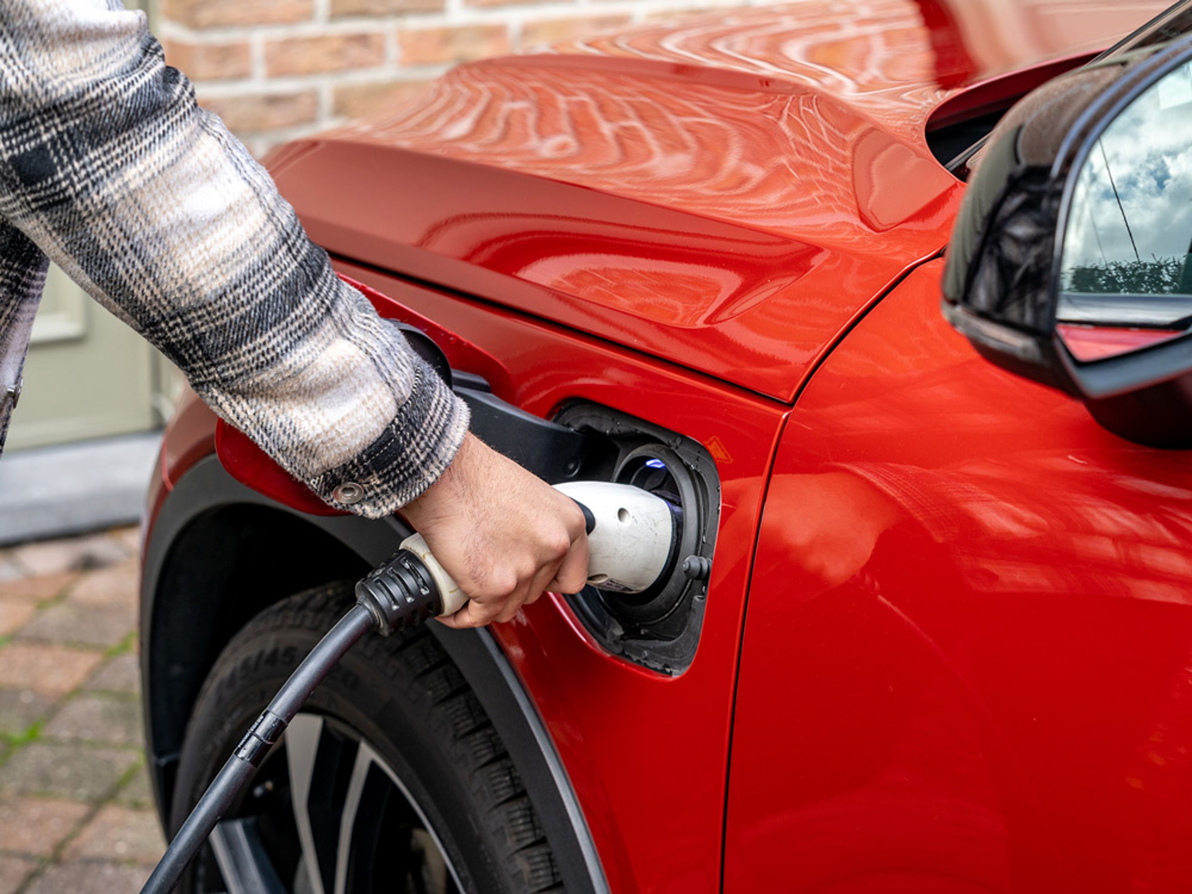 Une personne branche un câble de recharge dans une Volvo électrique rouge.