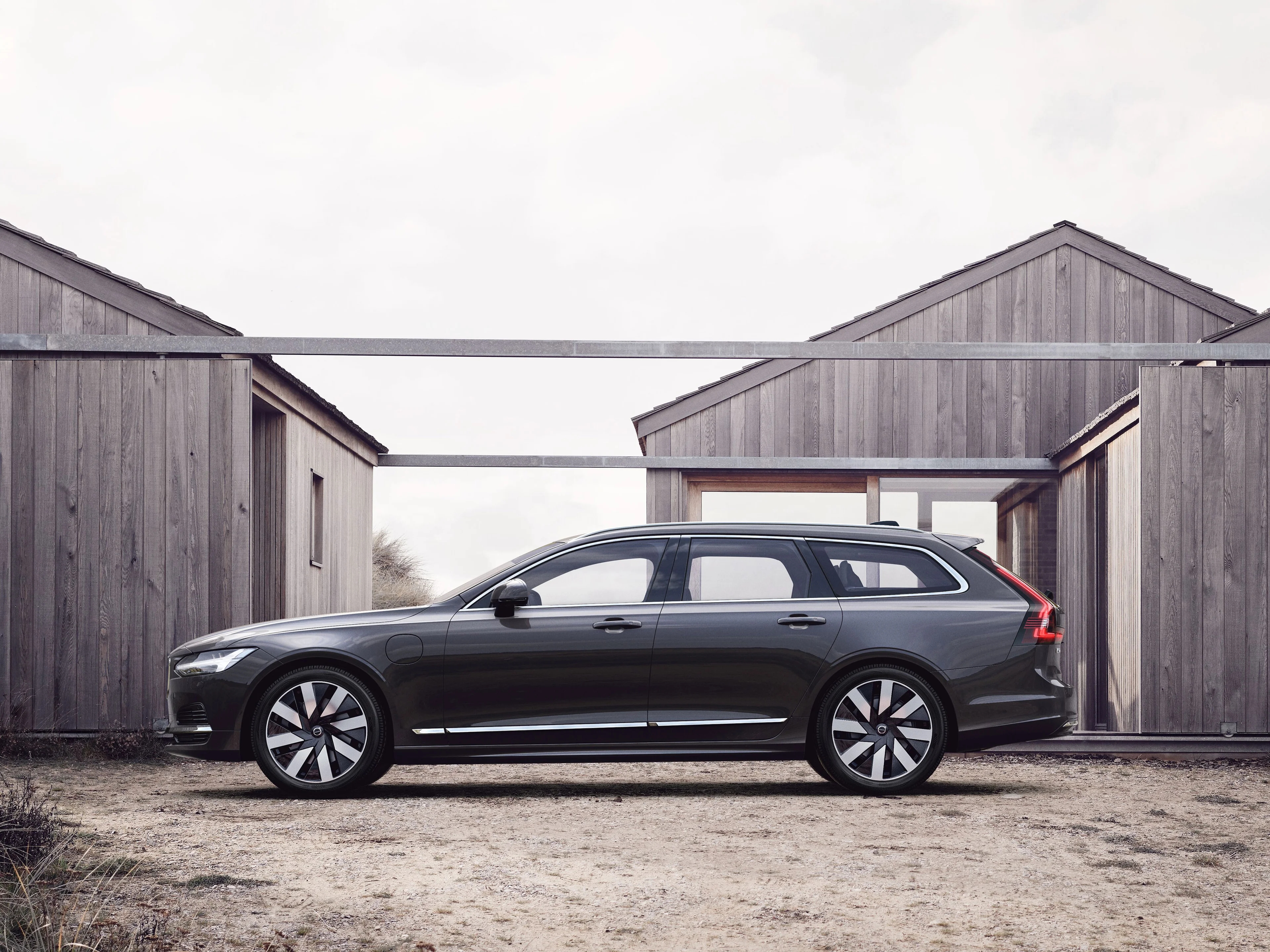 Ein blau-grauer Volvo V90 Kombi steht vor Holzhütten an einem Strand.