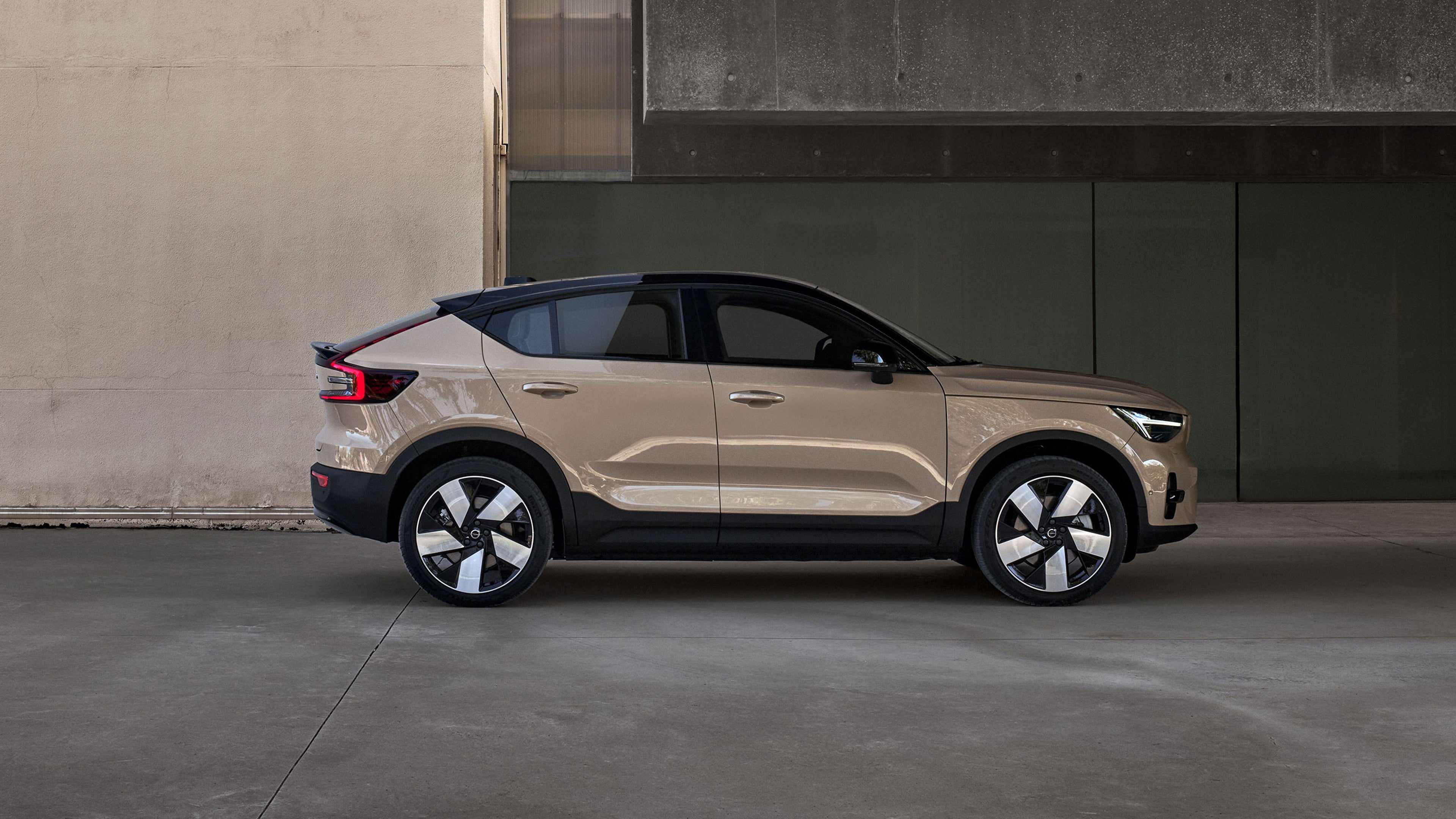 Volvo EC40 beige avec toit et bas de caisse noirs, garé devant un mur en béton, jantes bicolores au design distinctif.