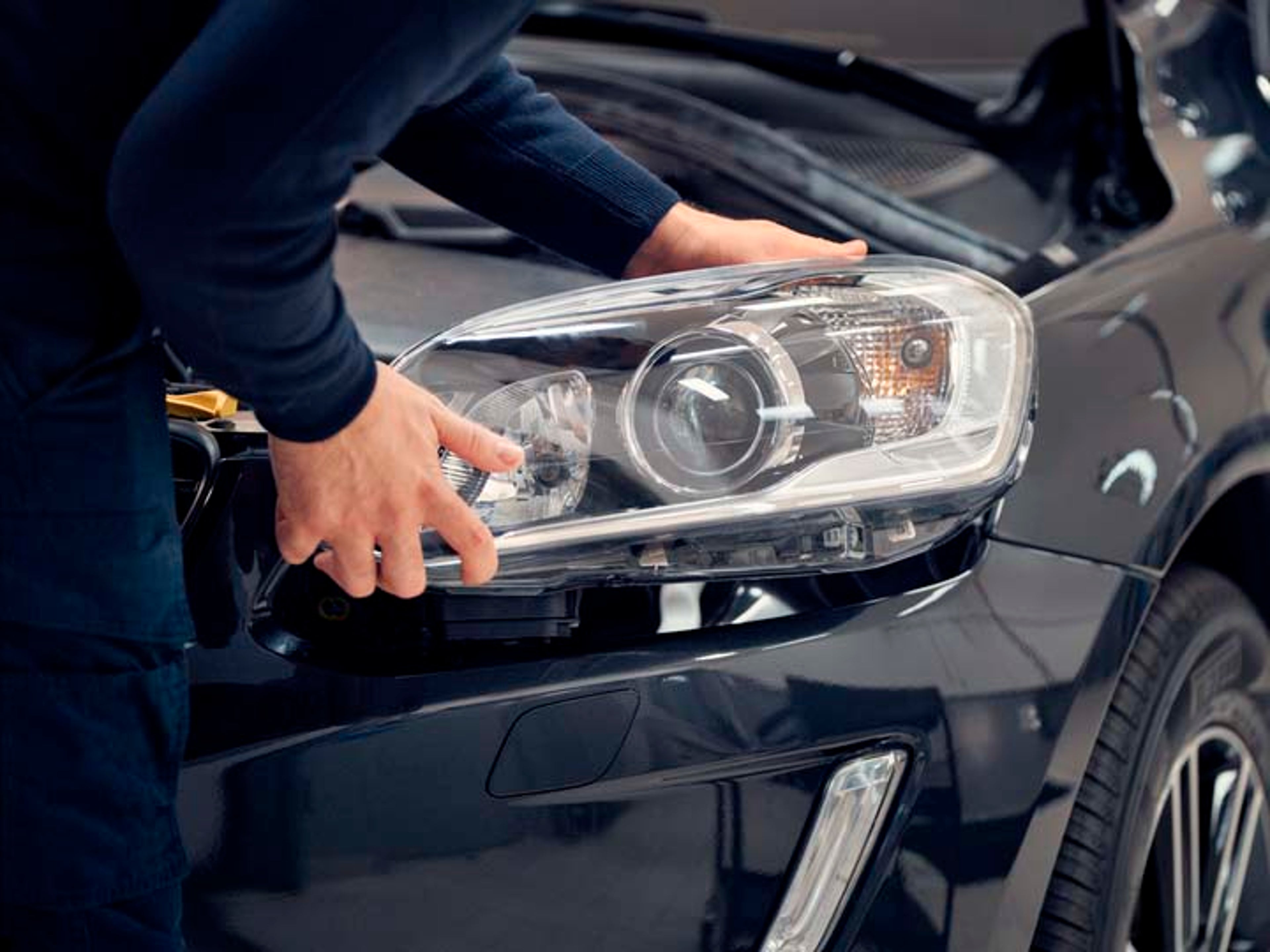 Un mecánico cambiando un faro de un vehículo Volvo con un recambio original