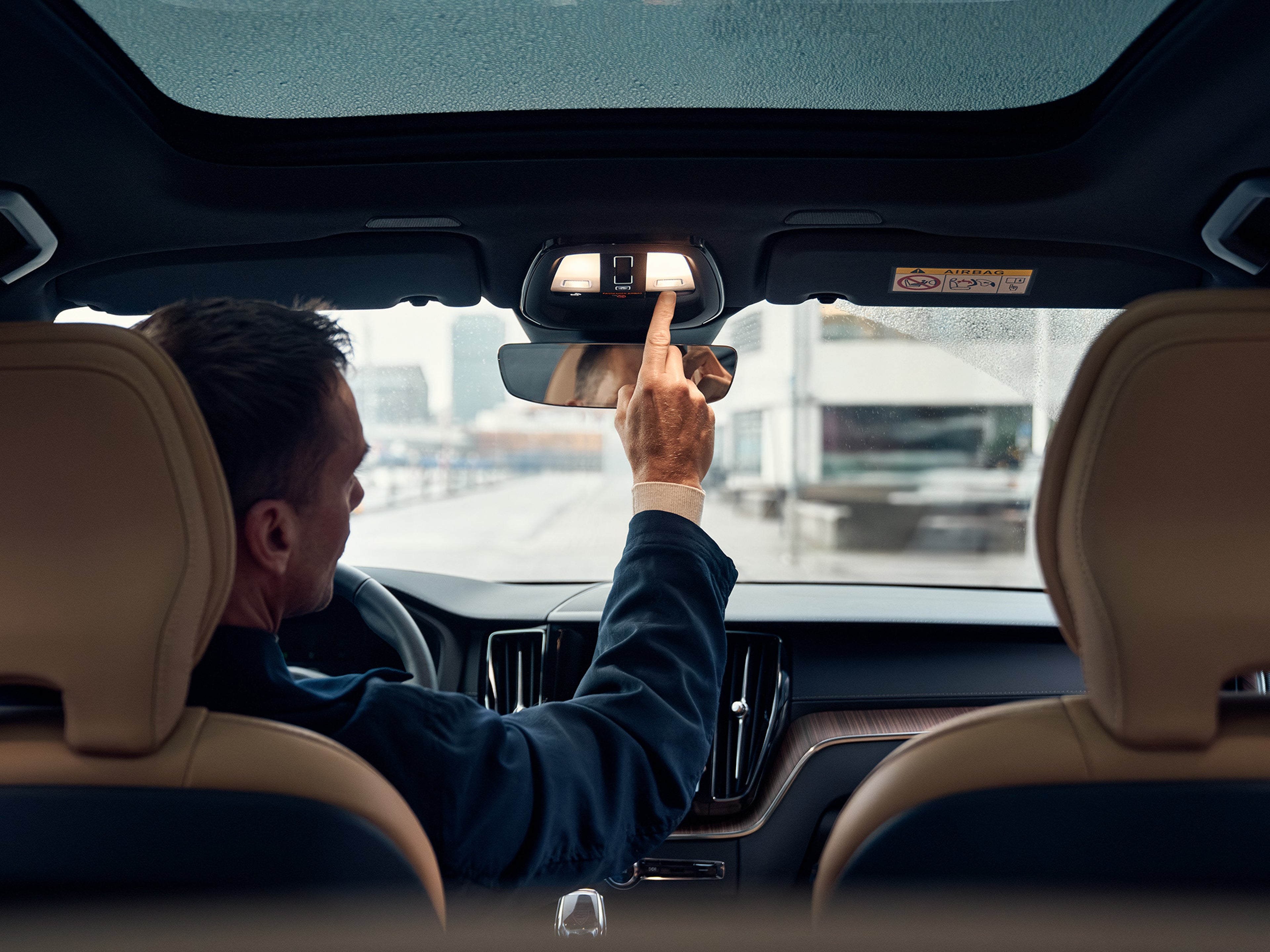 Mies istuu pysäköidyn Volvo -auton kuljettajan istuimella ja painaa kattokonsolin Volvo On Call -painiketta.
