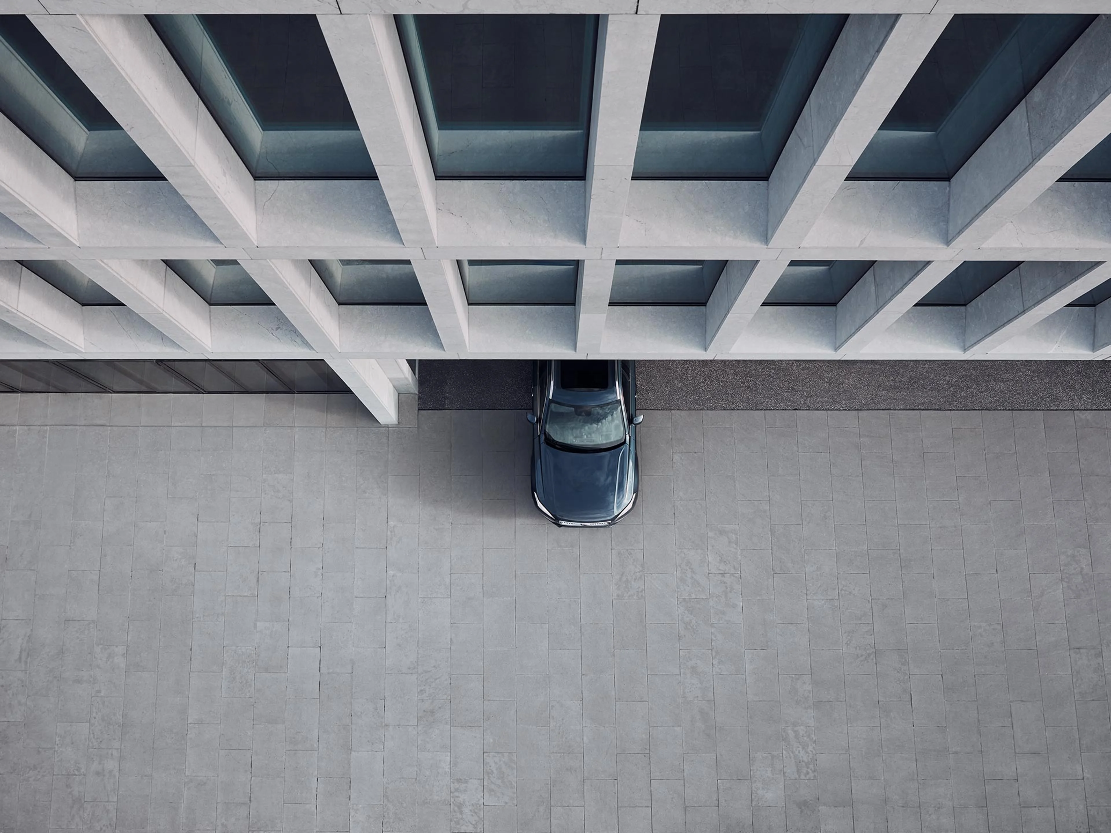 Vogelperspektive: die Front eines dunkelblauen Volvo XC90 ragt zur Hälfte aus der Ausfahrt eines modernen Hochhauses.