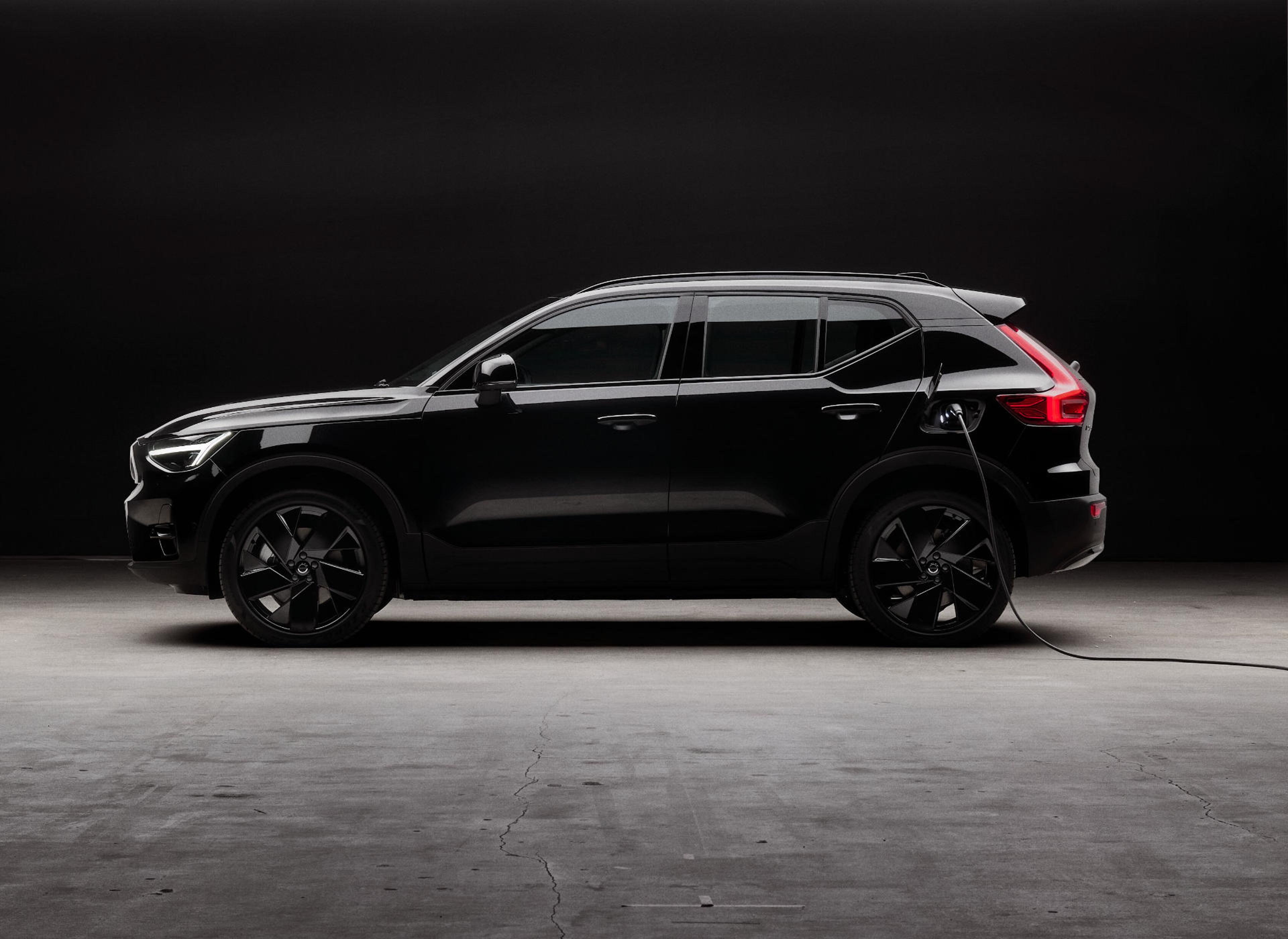 Seitenansicht eines tiefschwarzen Volvo EX40 SUV vor einer schwarzen Wand.