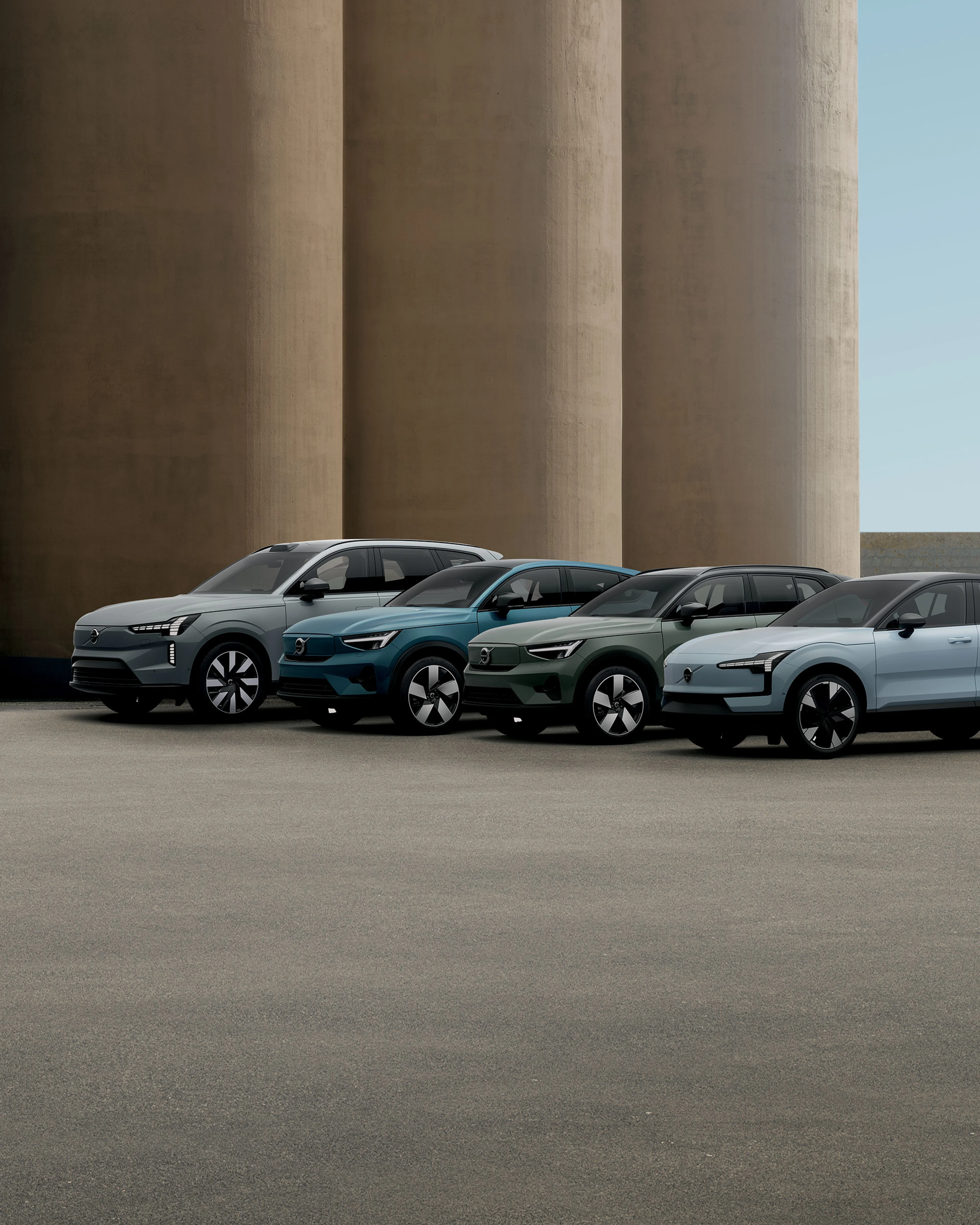 Quatre SUV modernes garés devant de grands piliers en béton par temps clair