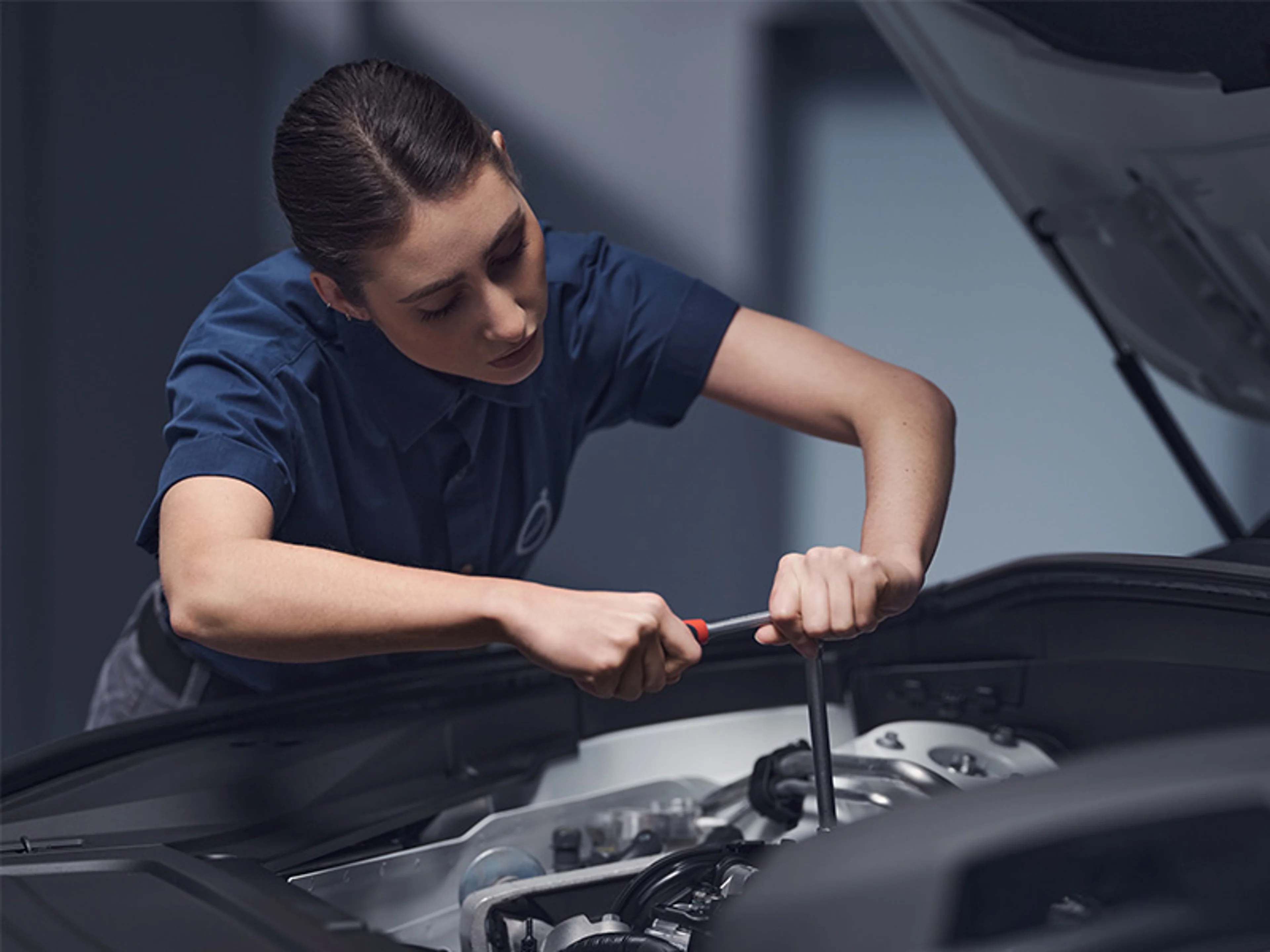 Une mécanicienne travaille sur le moteur d'une voiture avec une clé.
