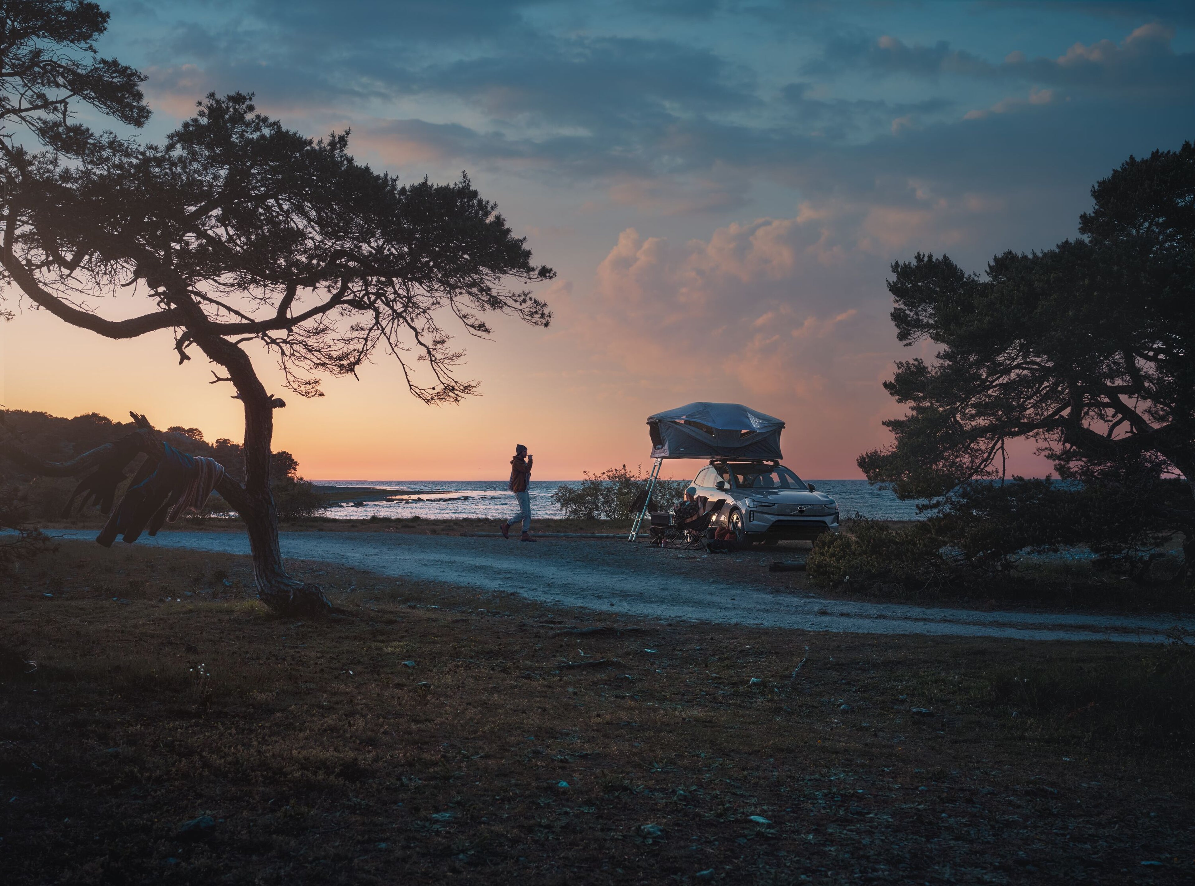 Two people beside Volvo car with roof tent and ladder in nature enjoying the sunset