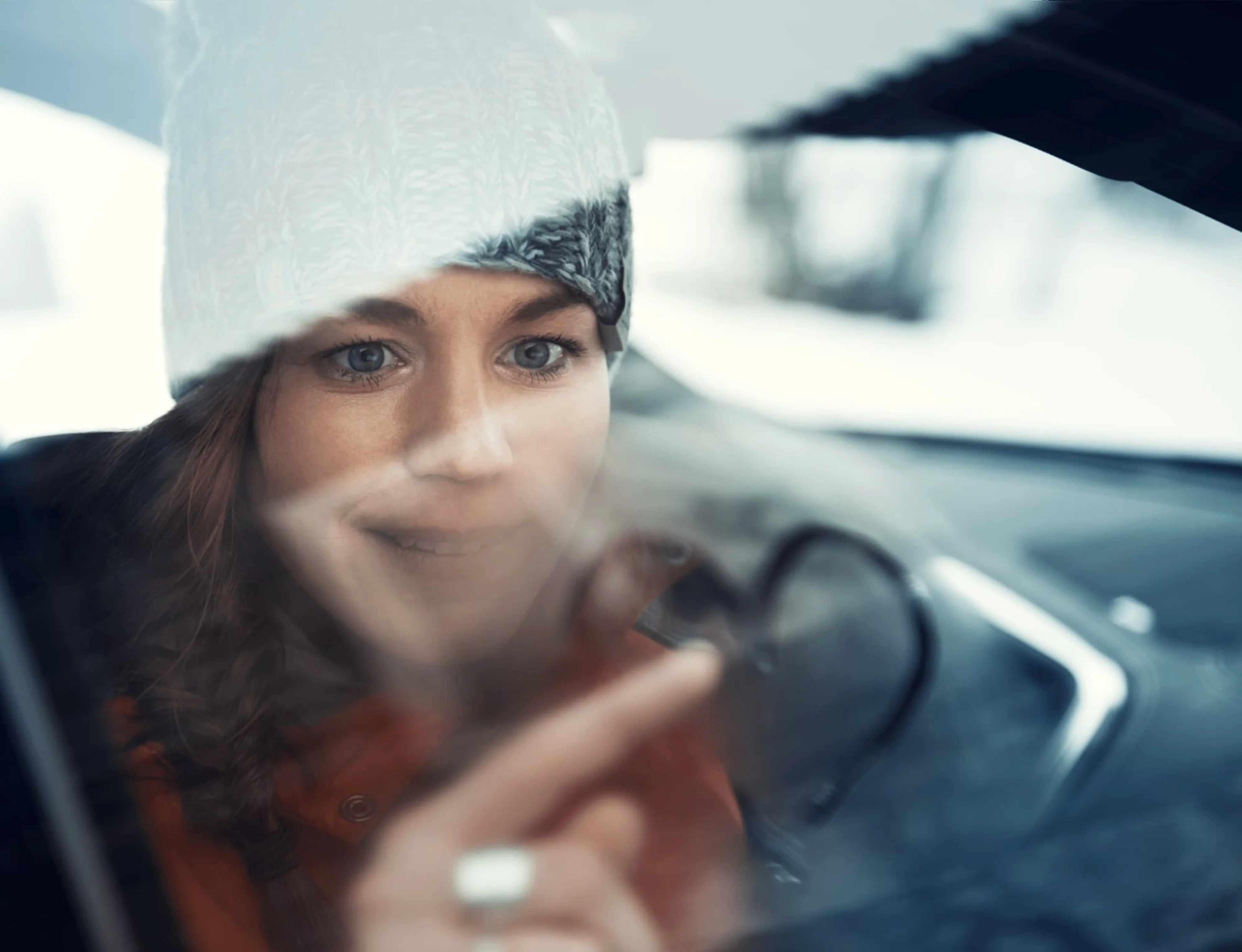 Une femme souriante en bonnet regardant à travers la vitre d'une voiture.