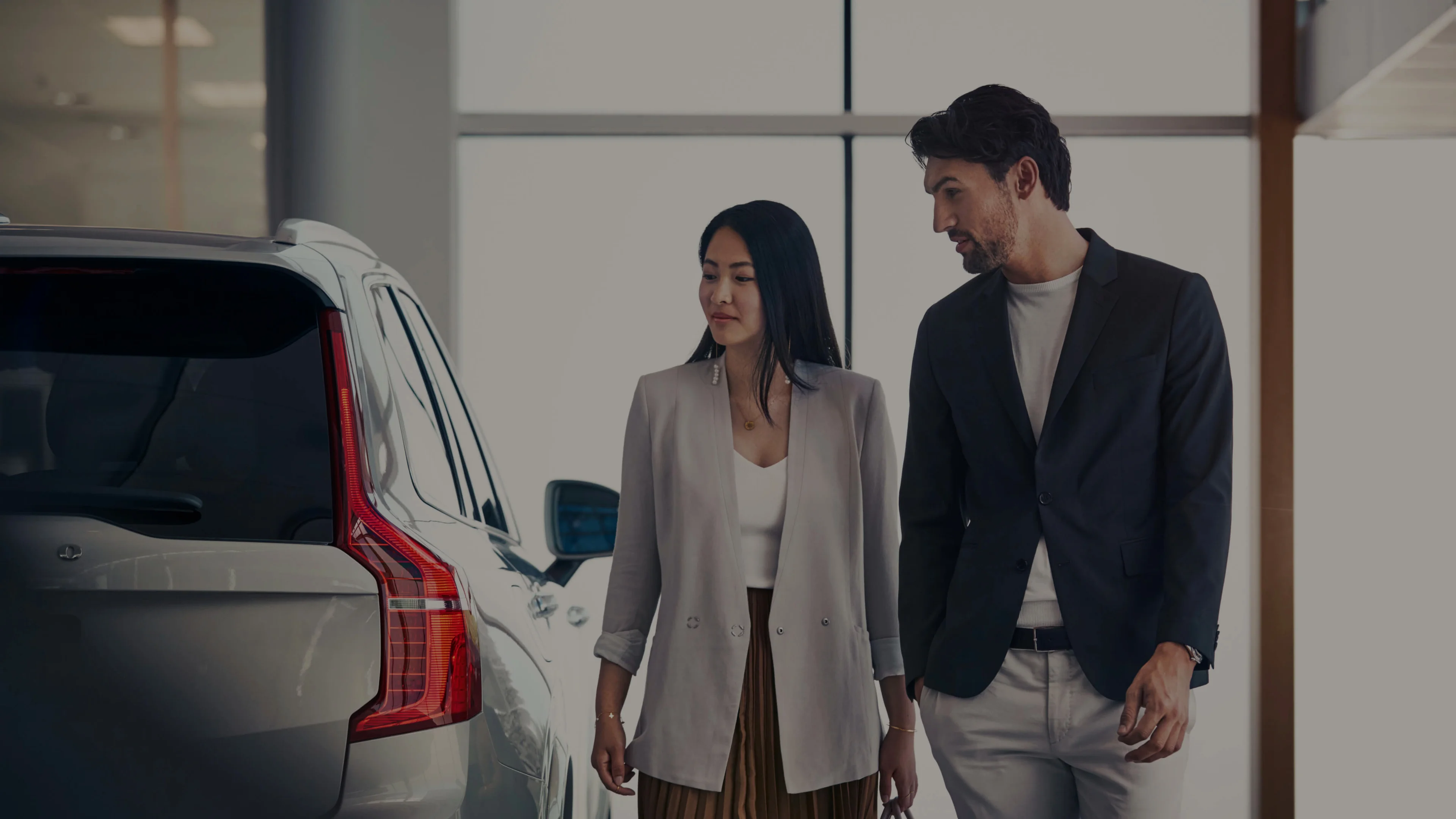 Zwei Personen begutachten einen Volvo in einem weißen Autohaus - Heckschuss