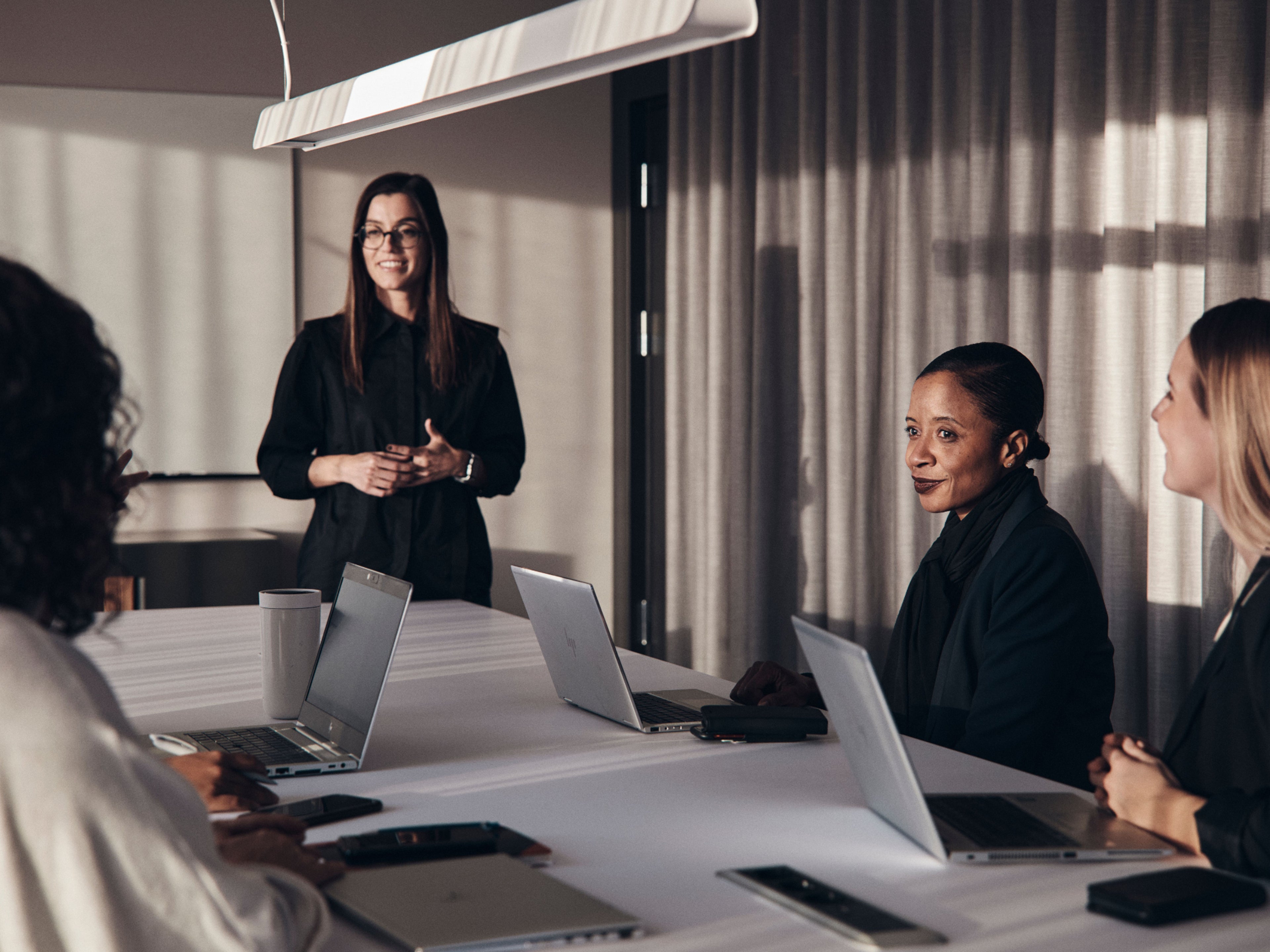 Fünf Frauen sitzen in einem Meetingraum an einem Tisch mit Laptops und sprechen miteinander.