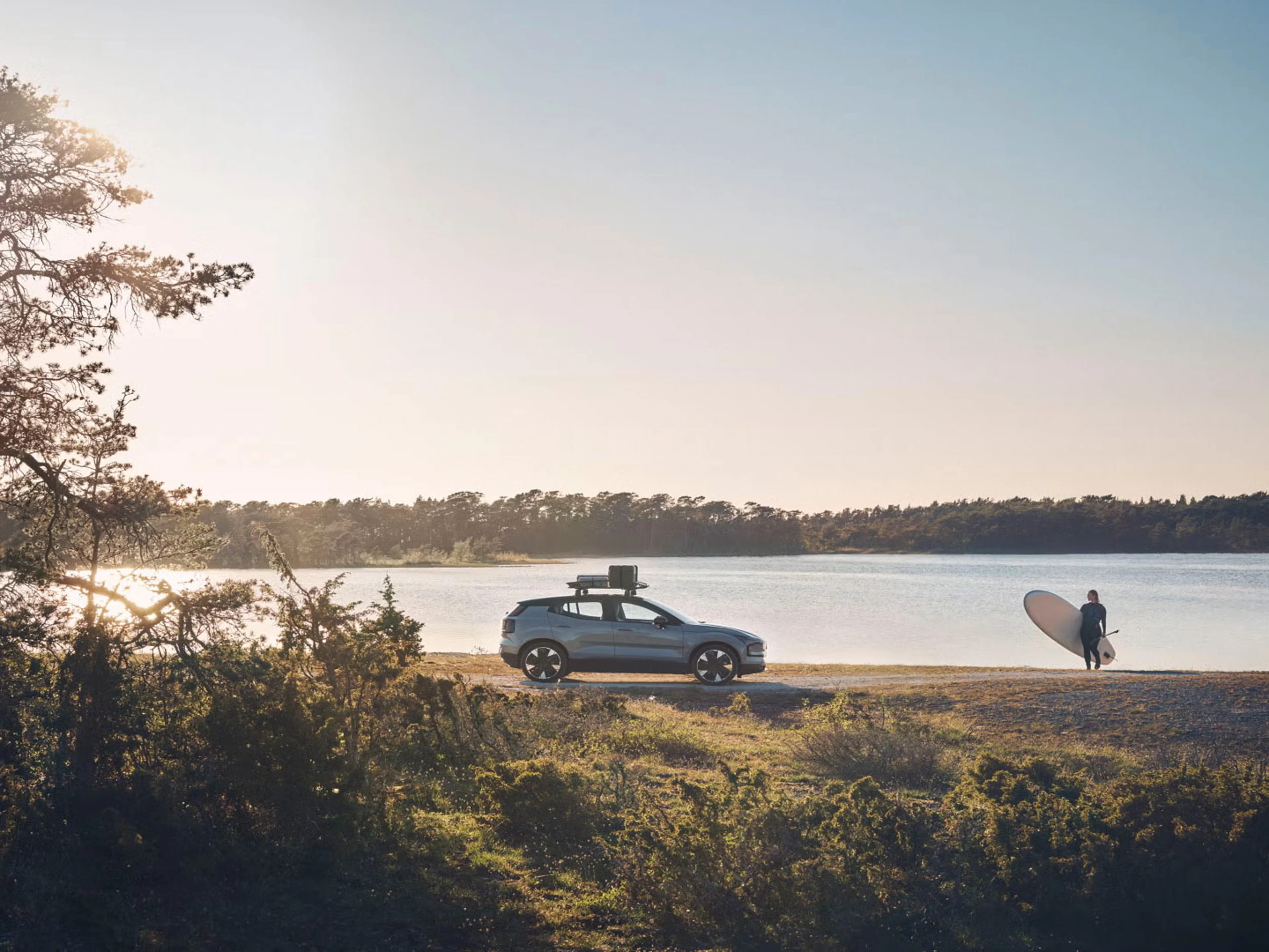 EX30 parked beside a lake with someone in a wetsuit and paddleboard approaching