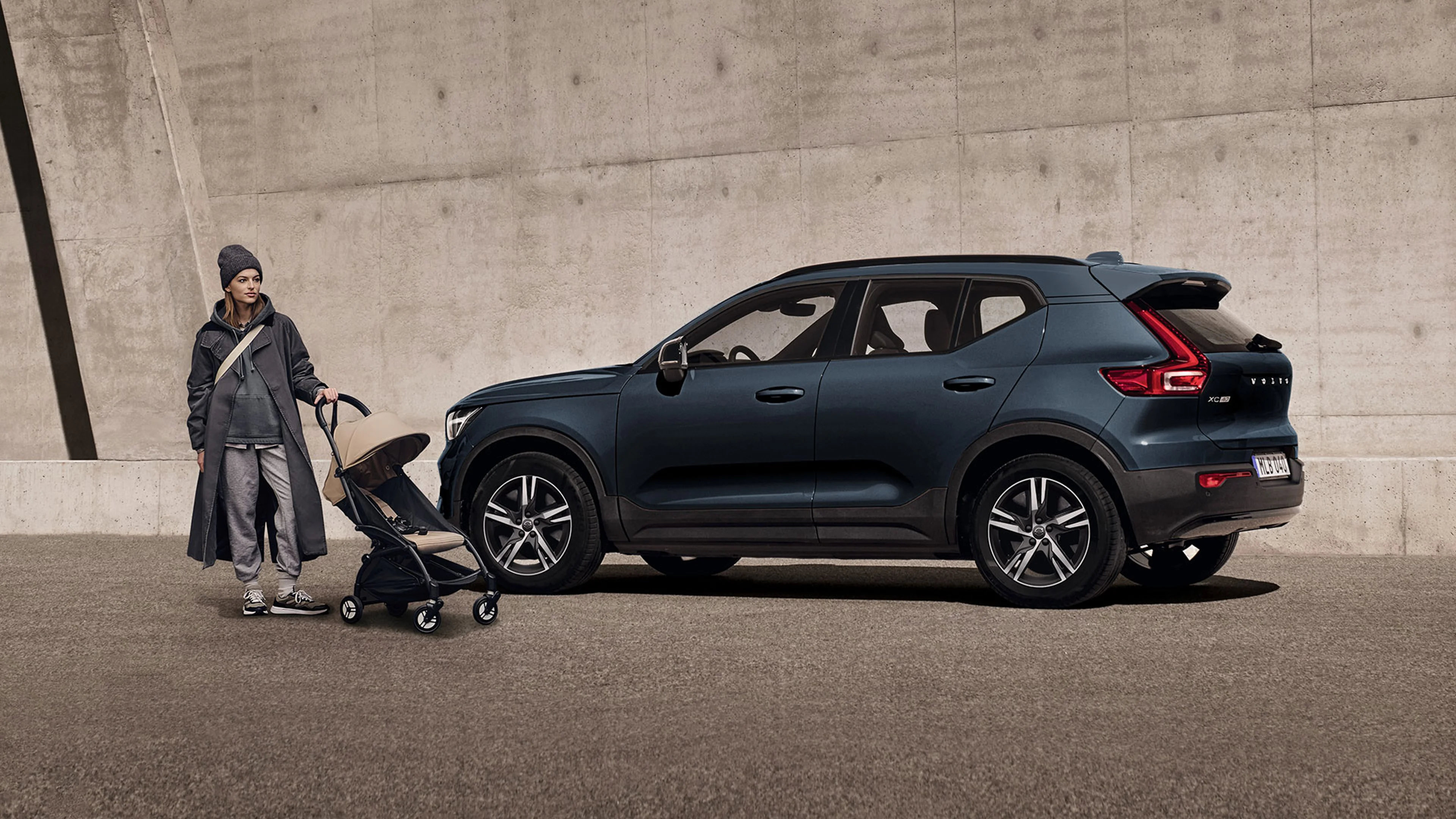 Femme avec une poussette à côté d’un Volvo XC40 bleu foncé devant un mur en béton