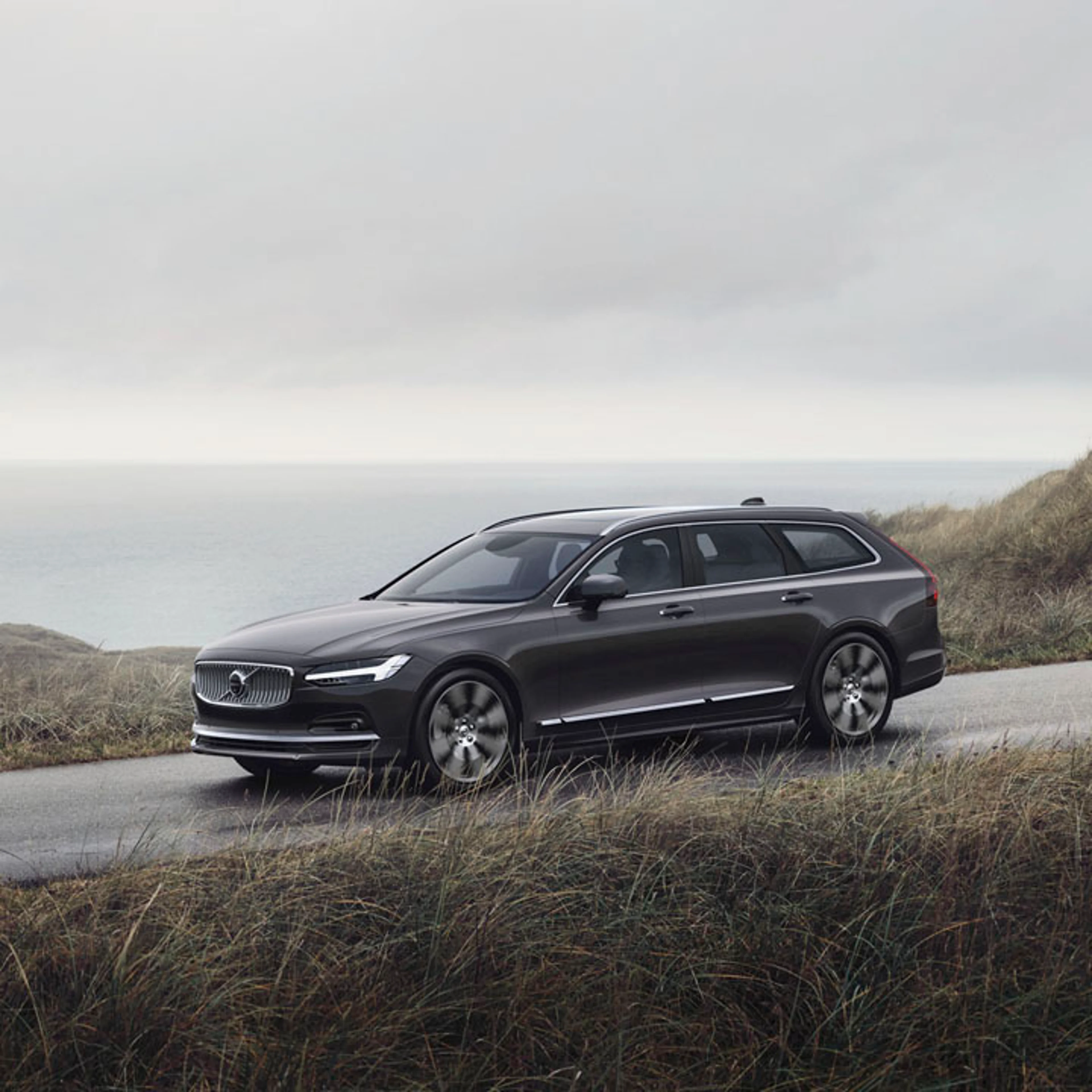 Volvo V90 vista lateral por una carretera junto al mar