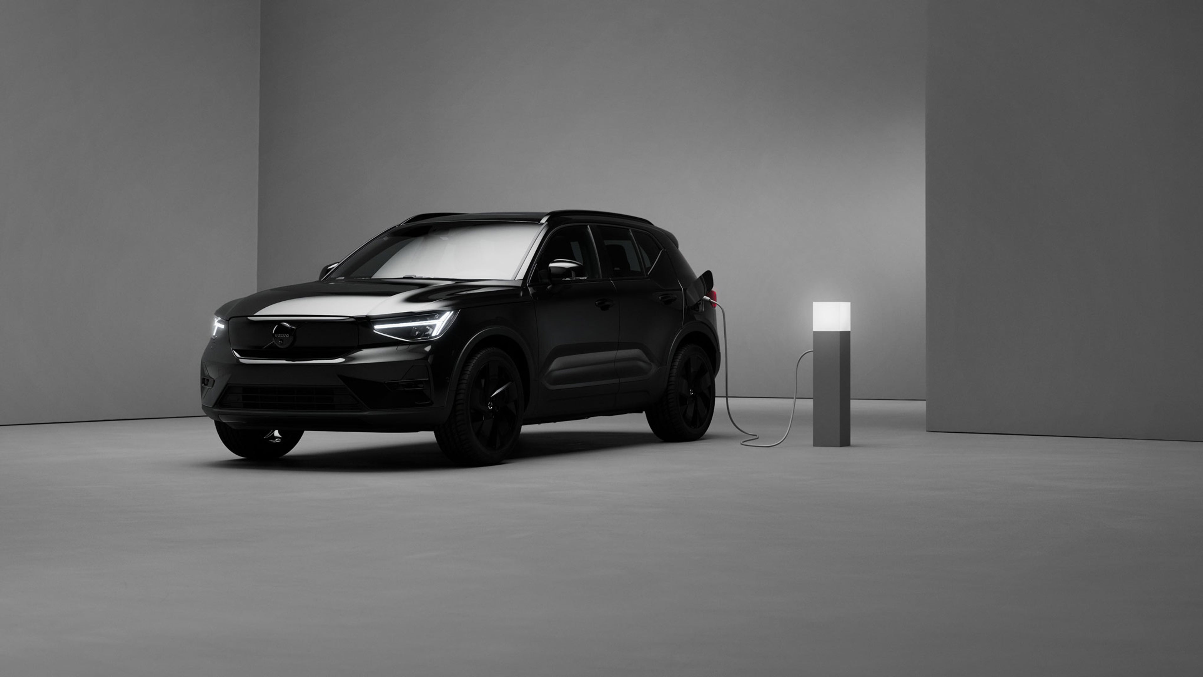 Volvo EX40 Black Edition branché à une borne, dans un décor minimaliste gris sombre et moderne