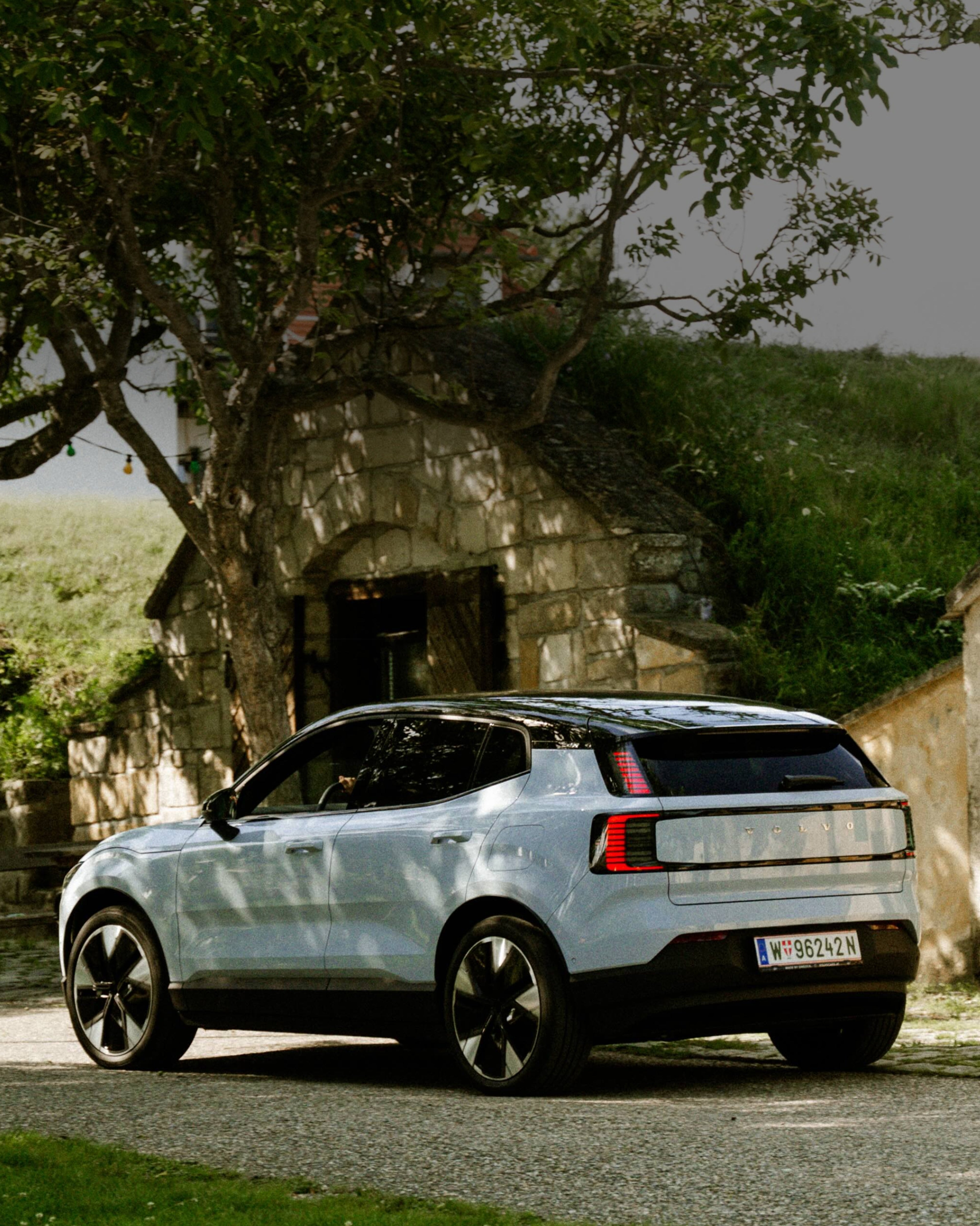 Rückansicht auf eines weißen Volvo EX30 mit schwarzem Dach, der zwischen ländlichen Häuser steht.