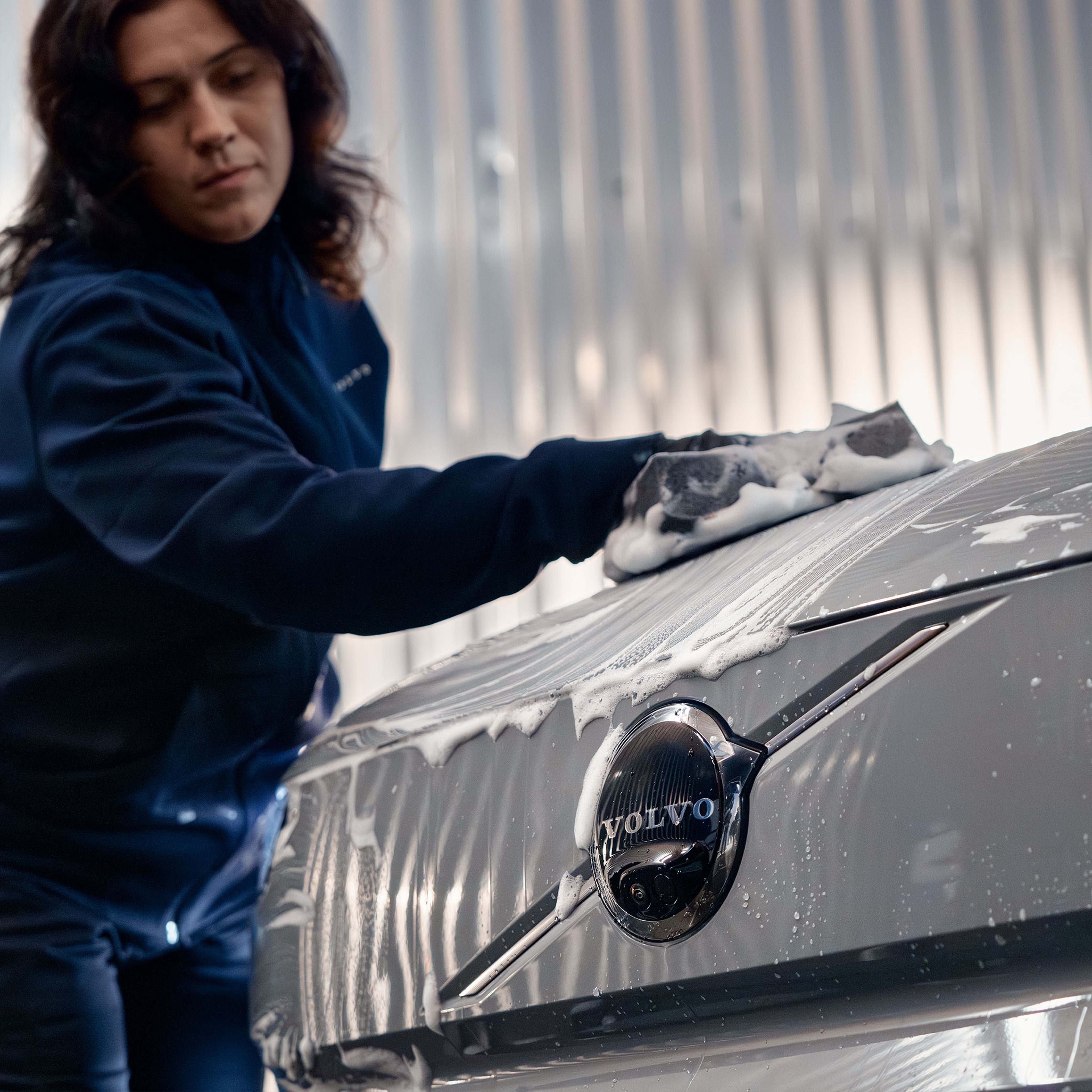 Volvo Omamekaanikko pesee käsin Volvon konepeltiä.