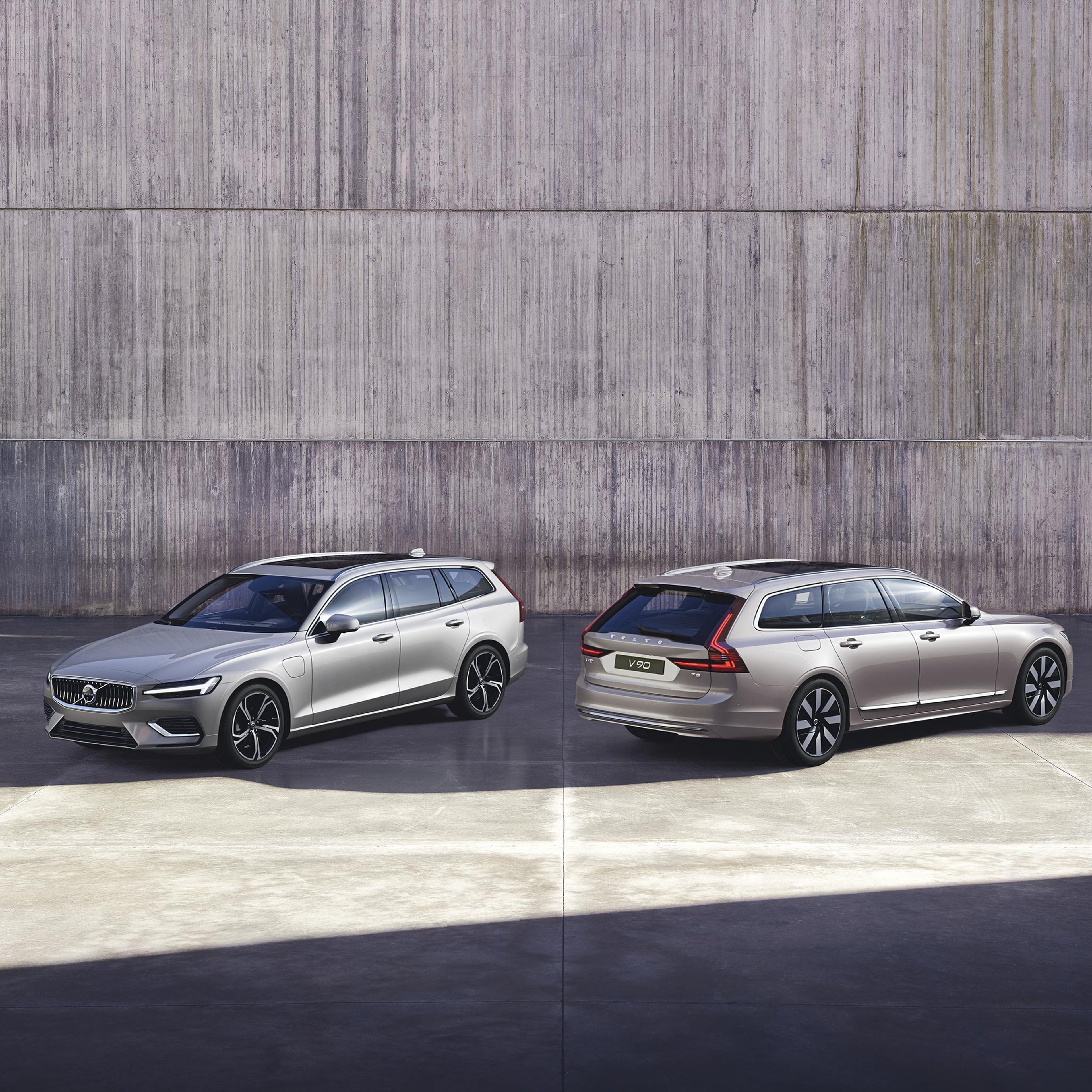 Volvo V60 ja V90 lataushybridifarmarit pysäköitynä viistoittain betoniseinän edustalle. V60 on kuvattu keula katsojaan päin ja V90 keula seinää kohden.