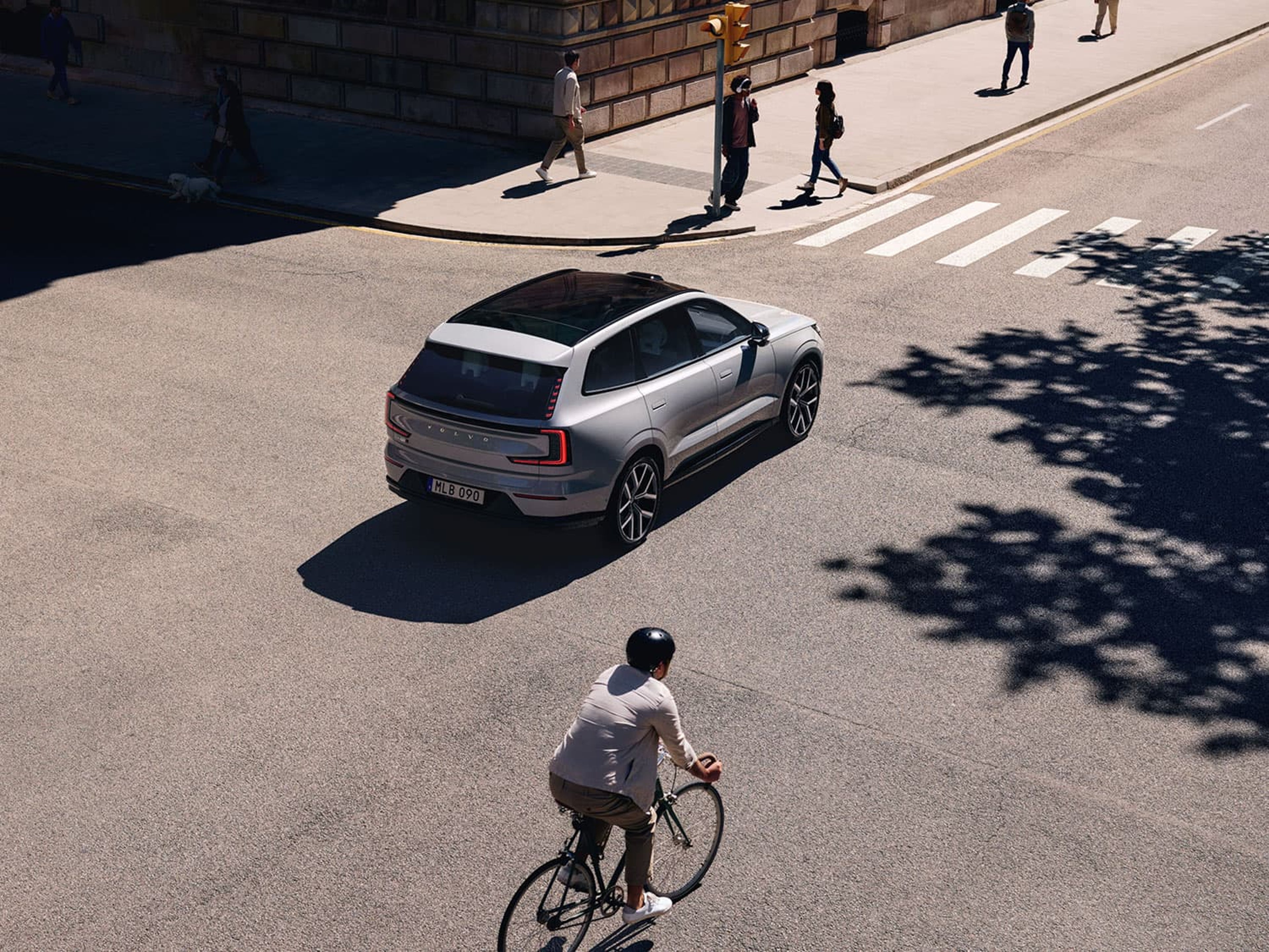 Une Volvo EX30 blanche traverse un carrefour, avec un cycliste au premier plan.