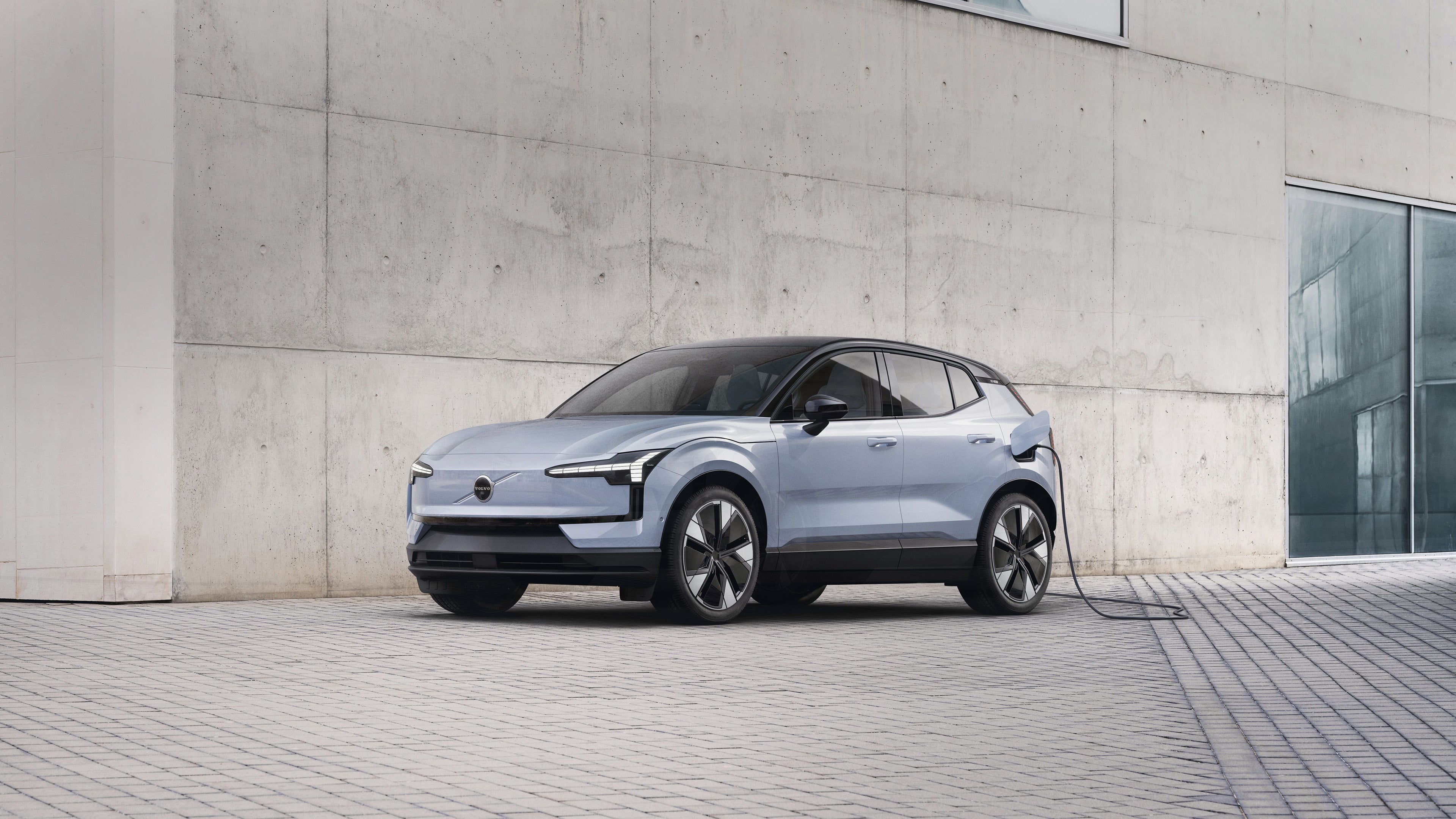 EX30 parked by a beige block wall with a charger plugged in