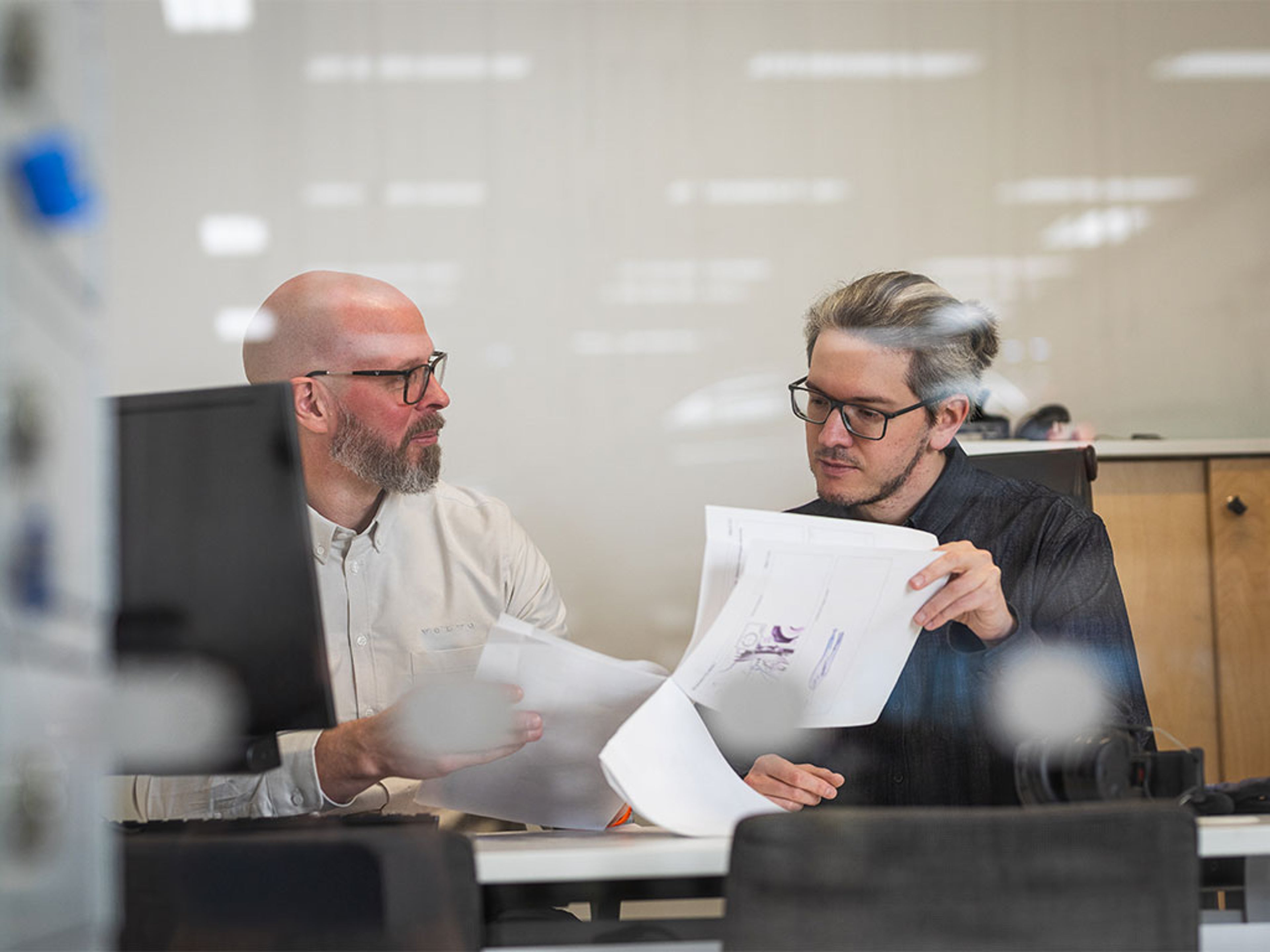 Dans son bureau, un concessionnaire feuillette un document en expliquant à son client comment bénéficier de l’aide famille nombreuse