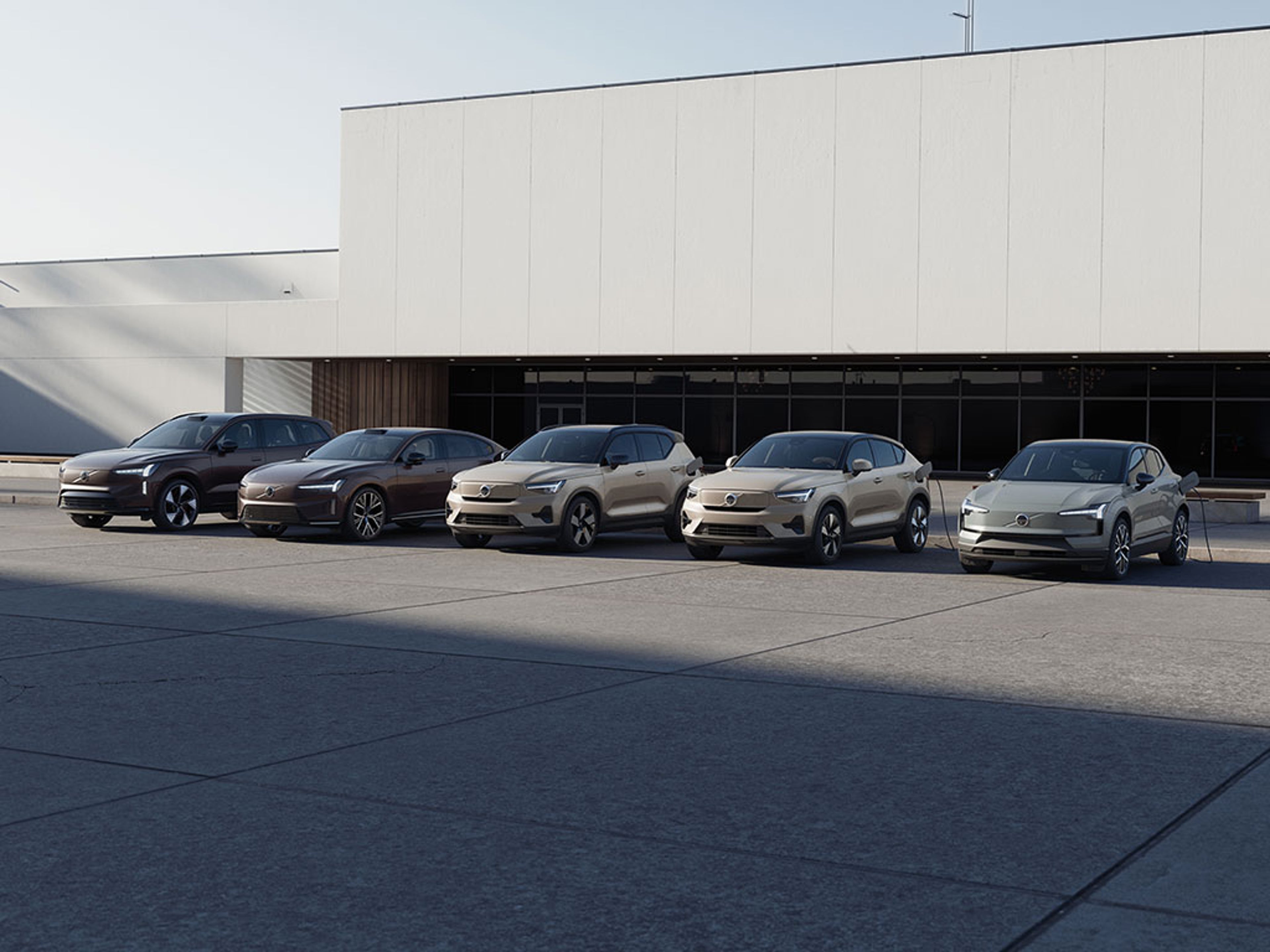 Cinq véhicules Volvo électriques garés devant un bâtiment moderne sur une surface en béton