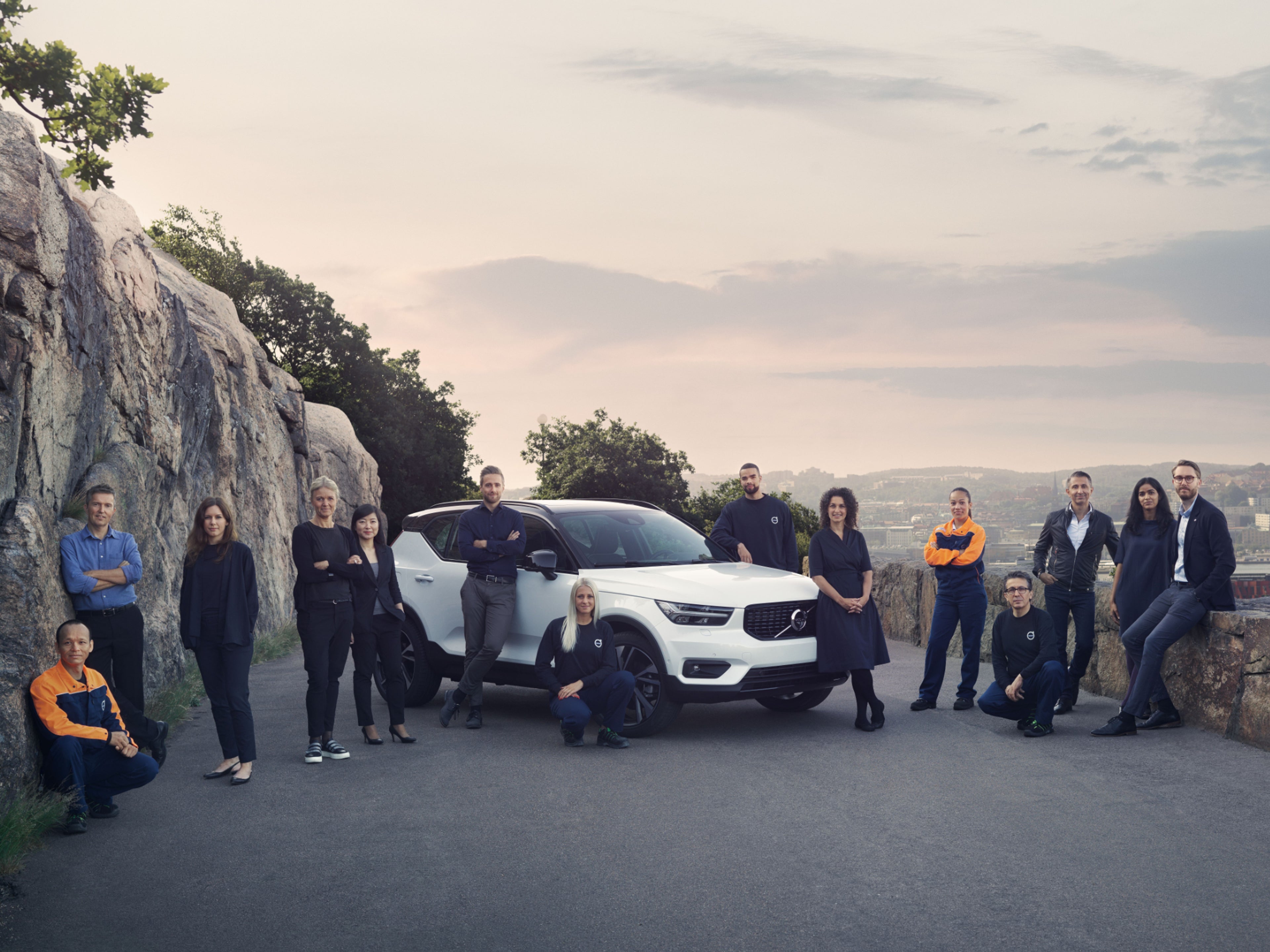 Sieben Männer und sechs Frauen stehen oder hocken vor einem weißen Volvo XC40.