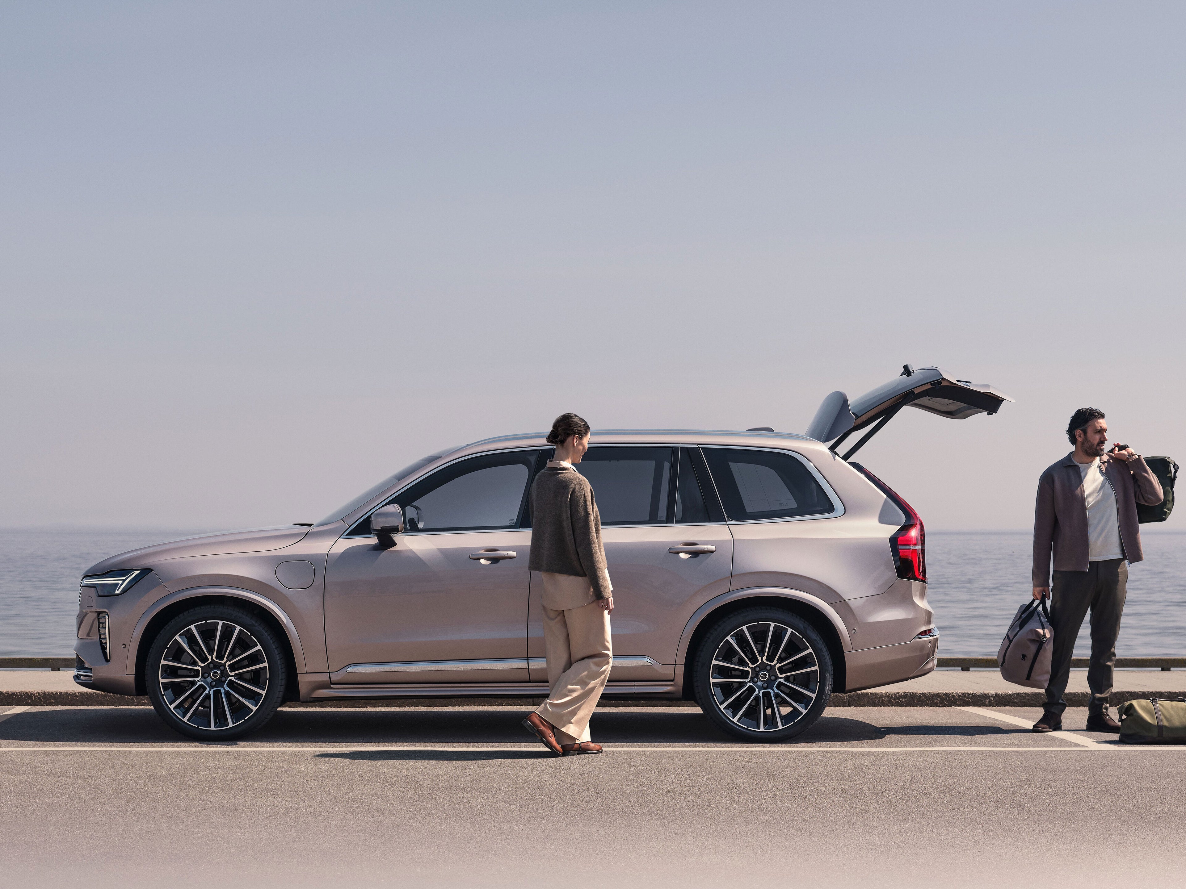 Zwei Personen stehen an einem silbernen Volvo XC90 SUV, der an einem See steht.