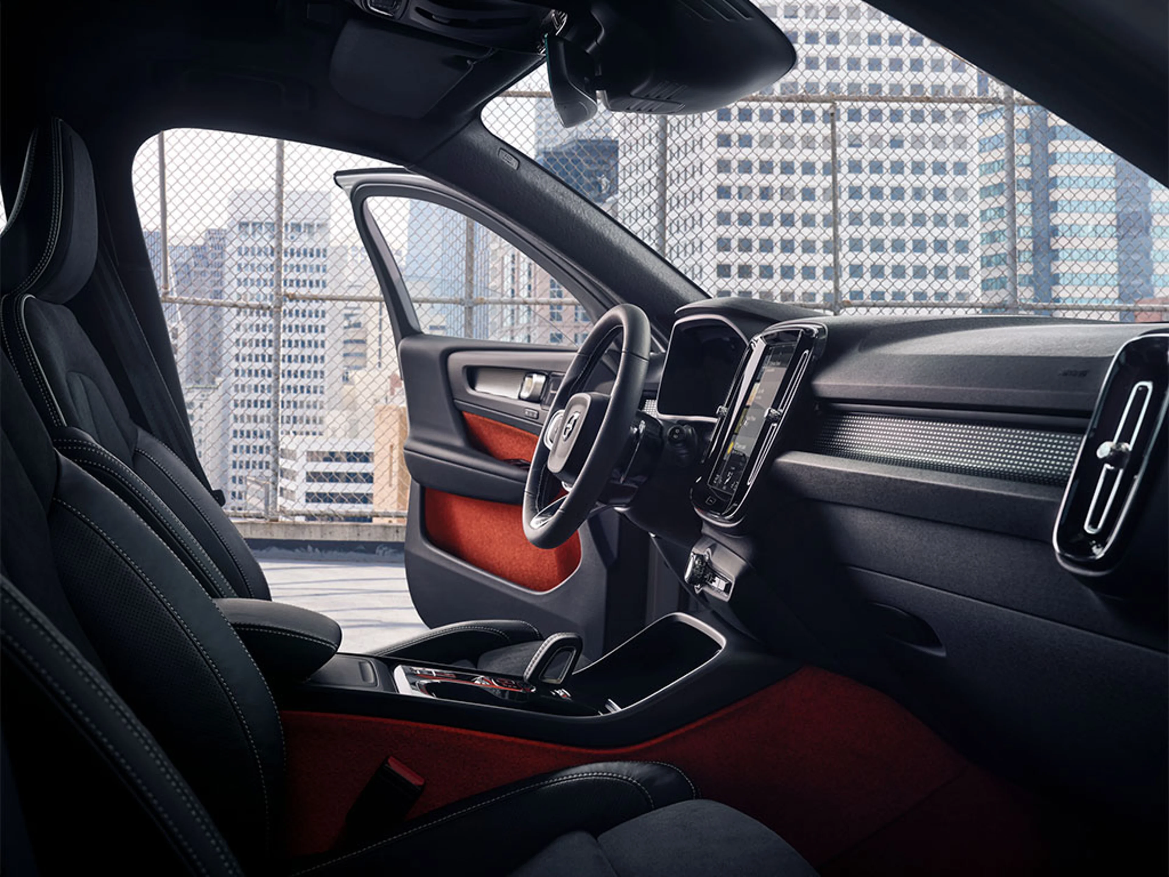 Intérieur d’une voiture moderne avec tableau de bord numérique, volant et vue sur des immeubles.