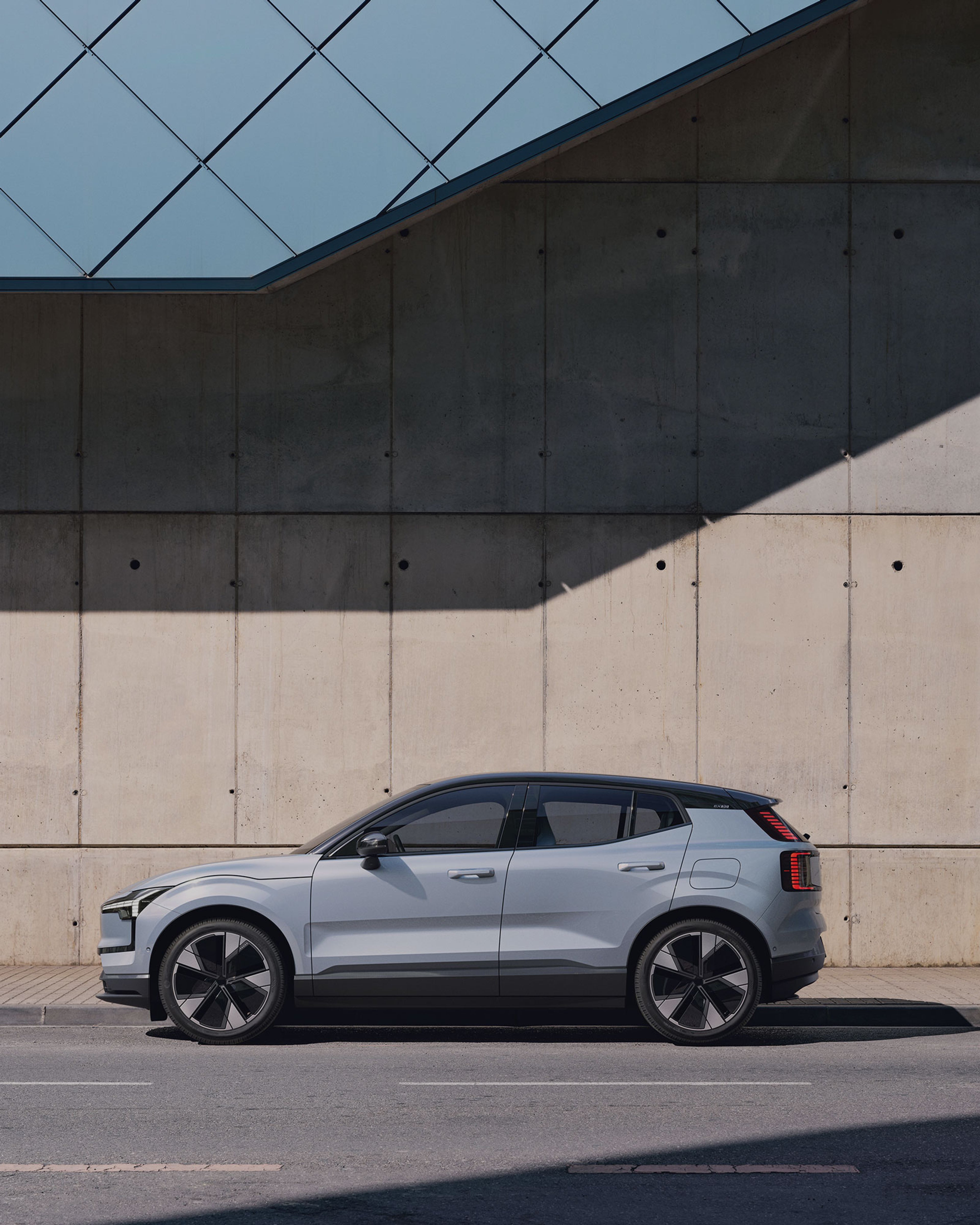 Vue latérale d'une Volvo EX30 grise avec toit noir garée dans la rue.