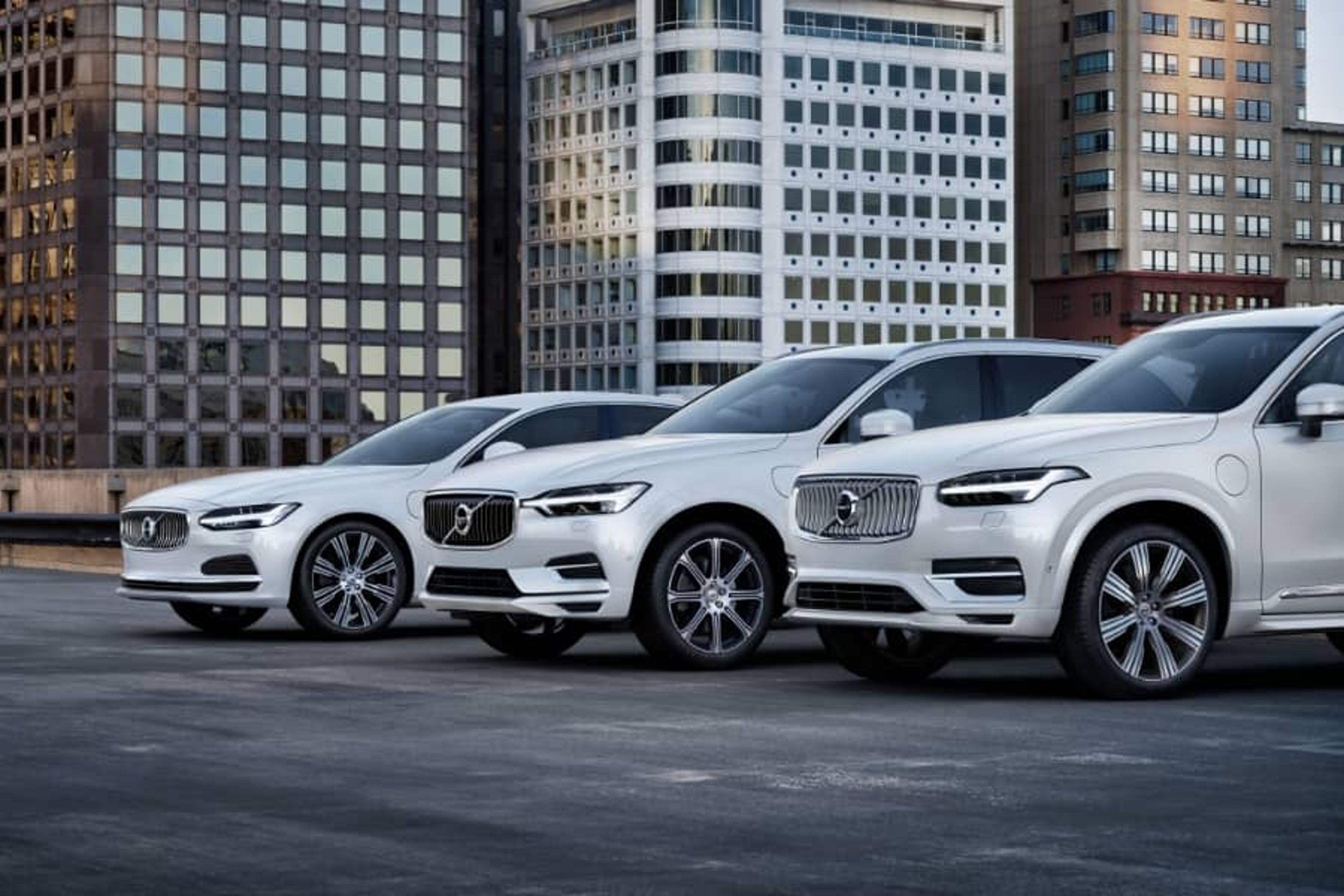 Tri bijela Volvo vozila parkirana ispred modernih poslovnih zgrada u urbanom okruženju.